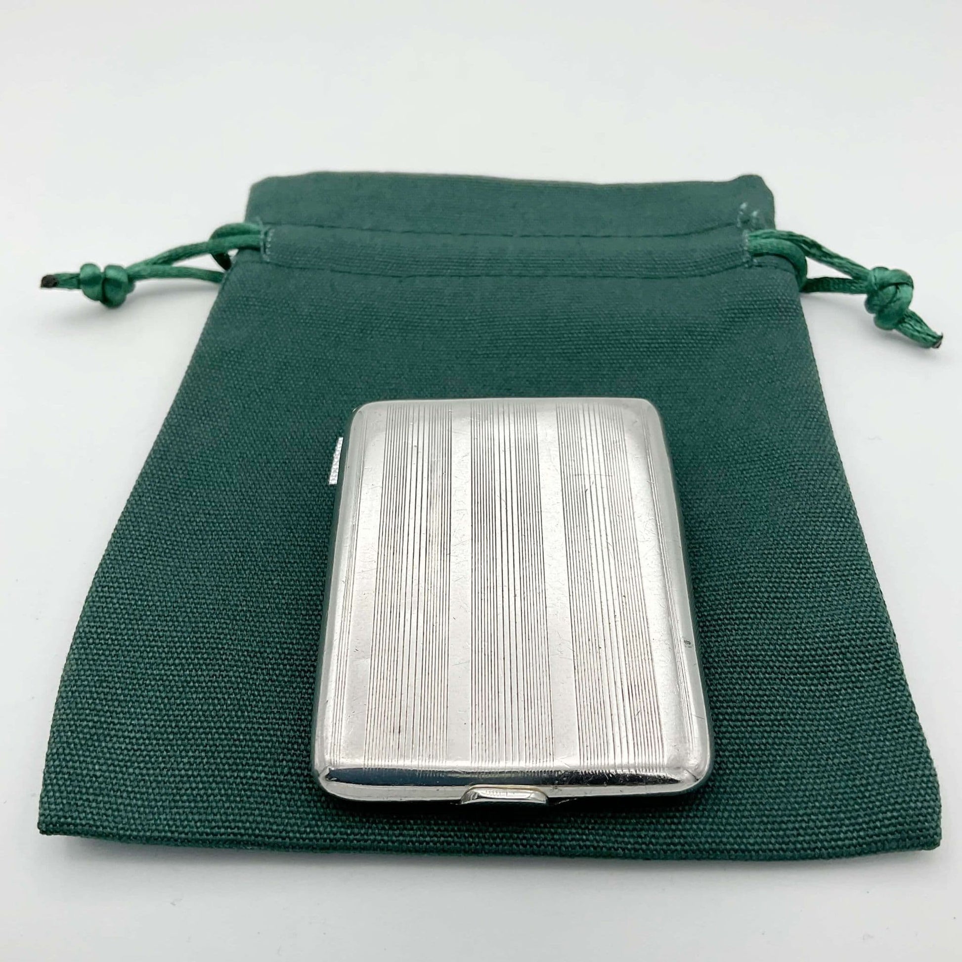 Back view of Silver matchbook case with a lined pattern on a green cotton bag.