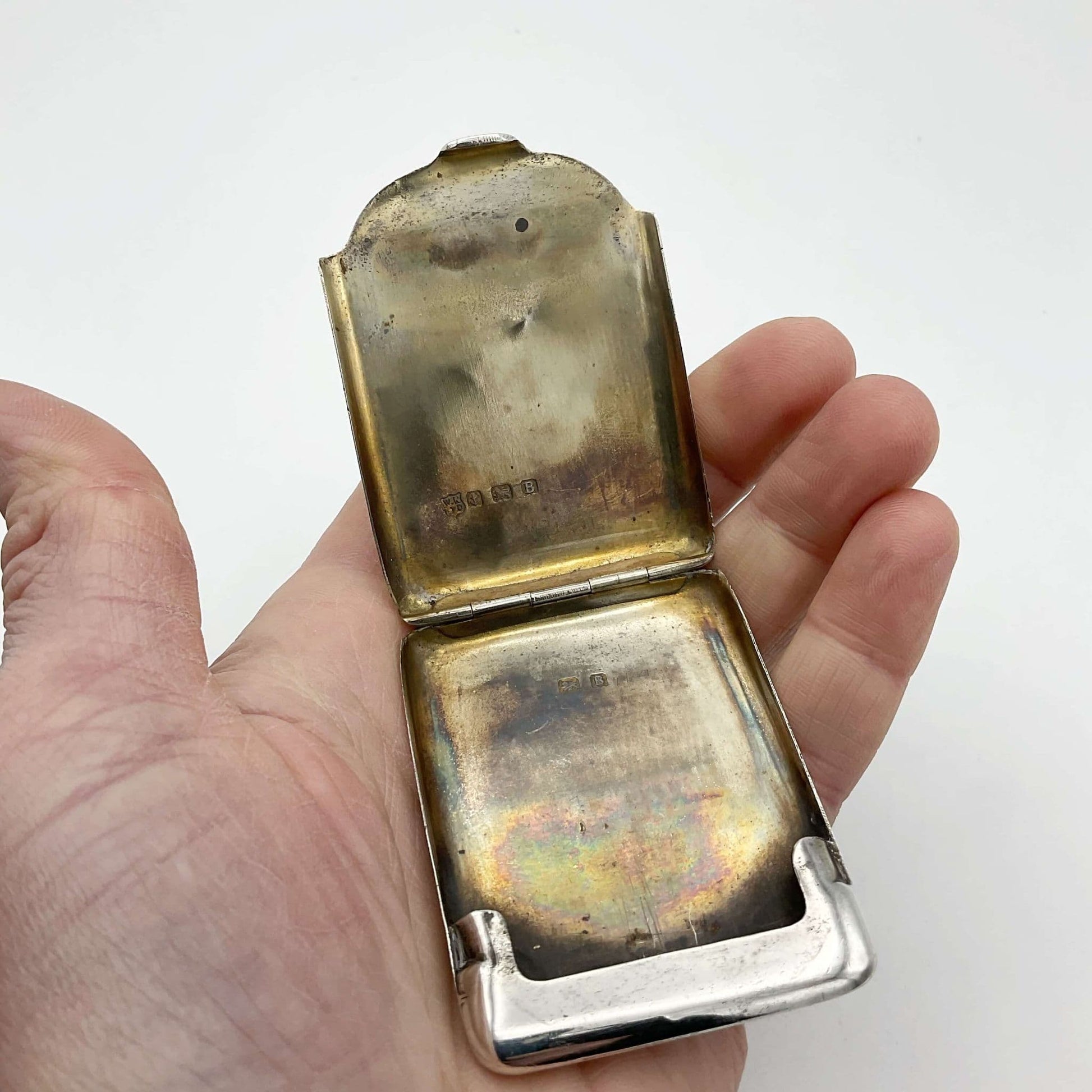 Silver matchbook case with the gilded interior showing held in a hand.
