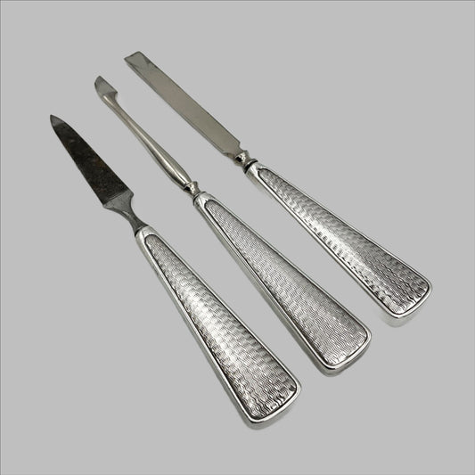 Three manicure tools with wavy 1930s design on the silver handles. The tools are a nail file and two types of cuticle pushers.