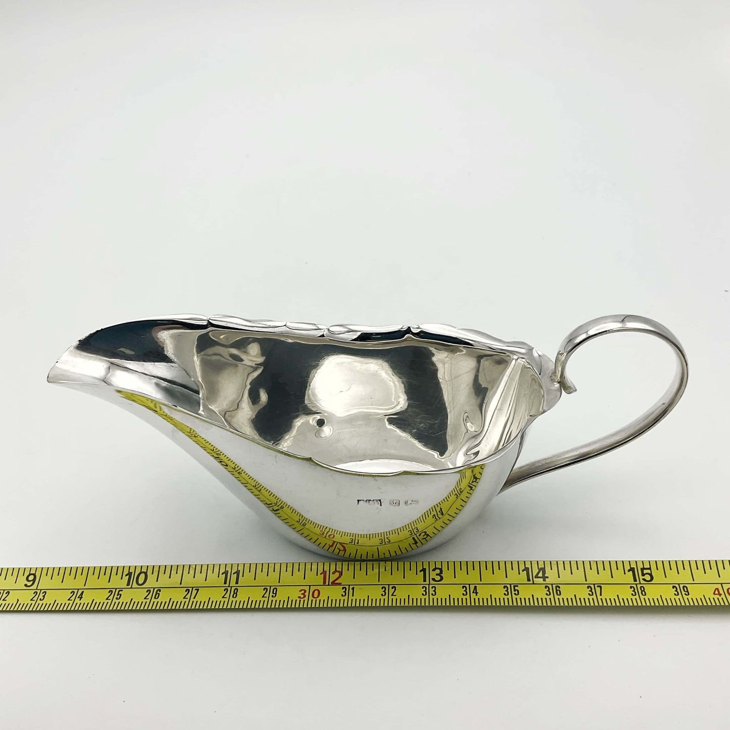 Silver sauce boat next to tape measure showing length as 15.5cm