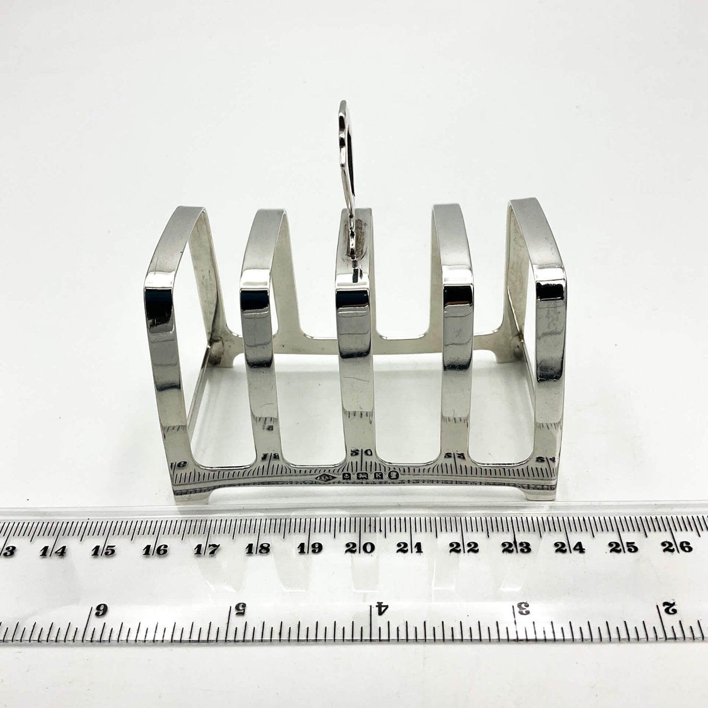 Art deco style silver toast rack on a white background next to ruler measuring 8cm