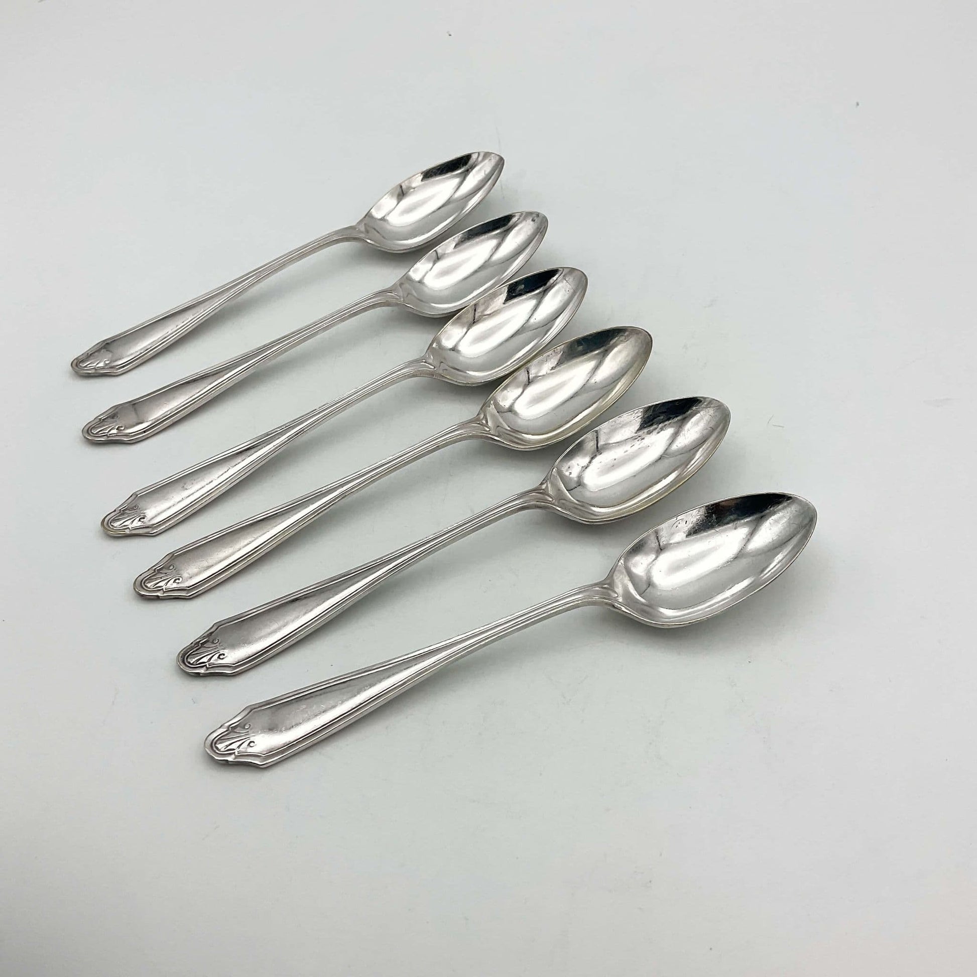 Six silver plated vintage coffee spoons on a plain background