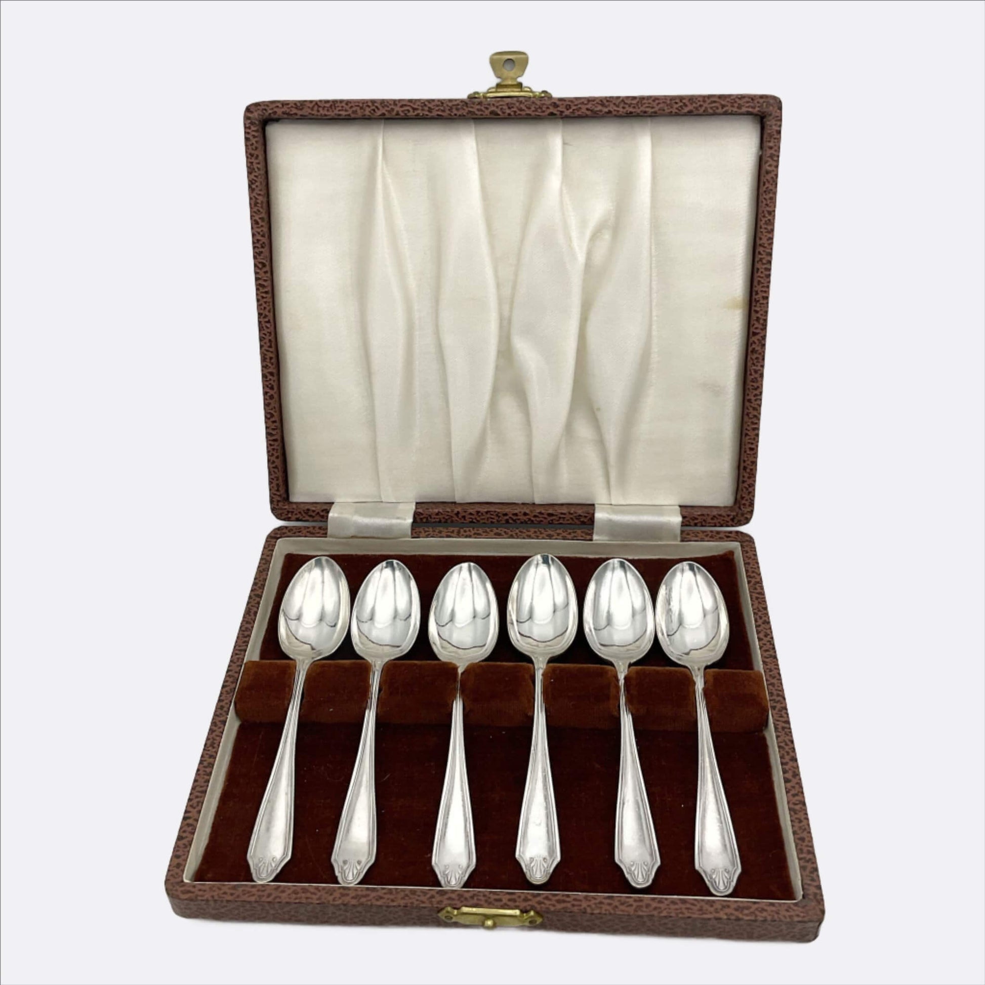 A set of six silver coffee spoons displayed inside an open brown presentation box with a cream satin lining, on a light gray background.