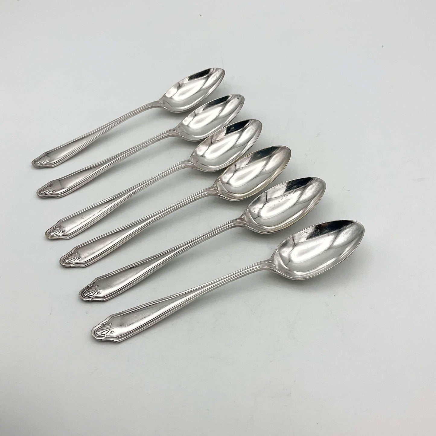 Six polished silver coffee spoons arranged diagonally on a light gray background.