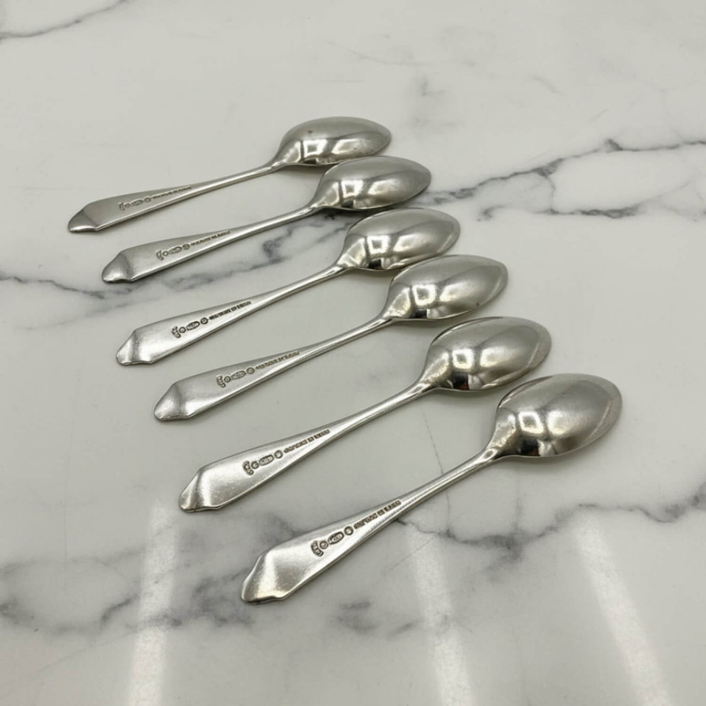 Five polished silver coffee spoons arranged diagonally on a white marble surface with gray veining.