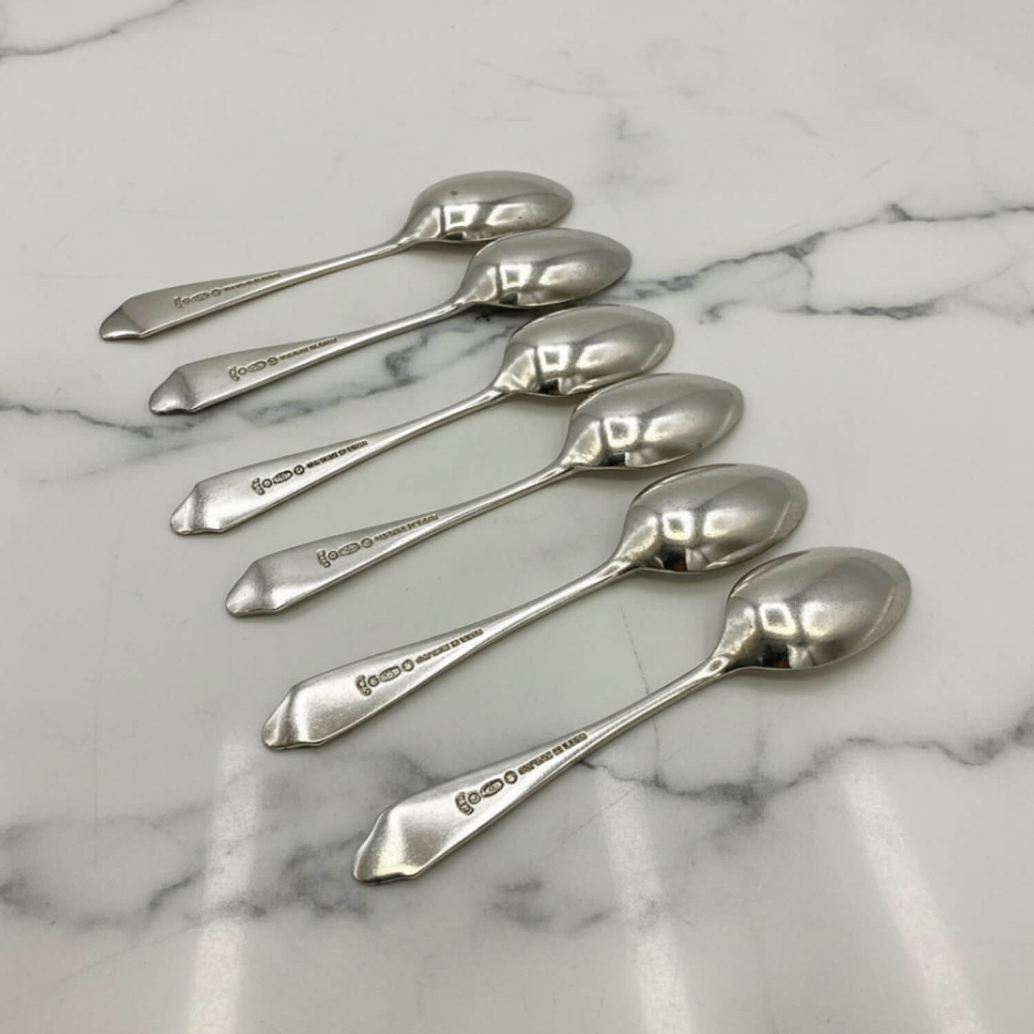 Five polished silver coffee spoons arranged diagonally on a white marble surface with gray veining.
