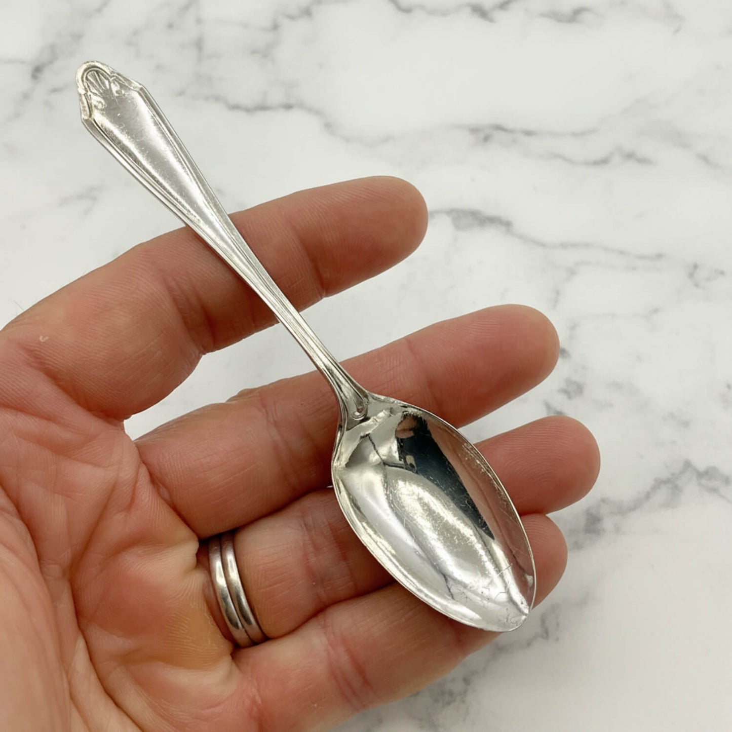 1950s Vintage Silver Plated Coffee Spoon held in a hand with a marble background
