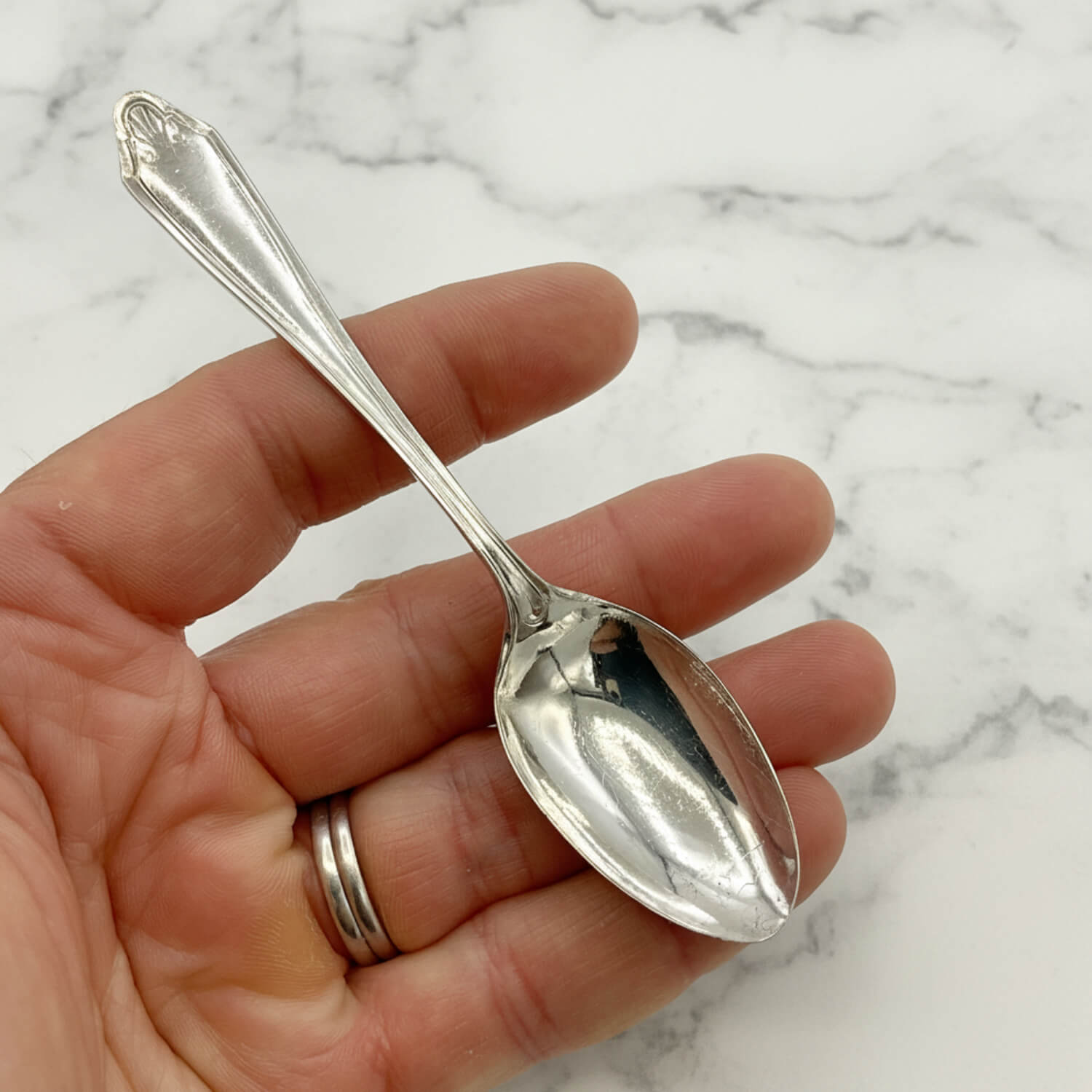 1950s Vintage Silver Plated Coffee Spoon held in a hand with a marble background