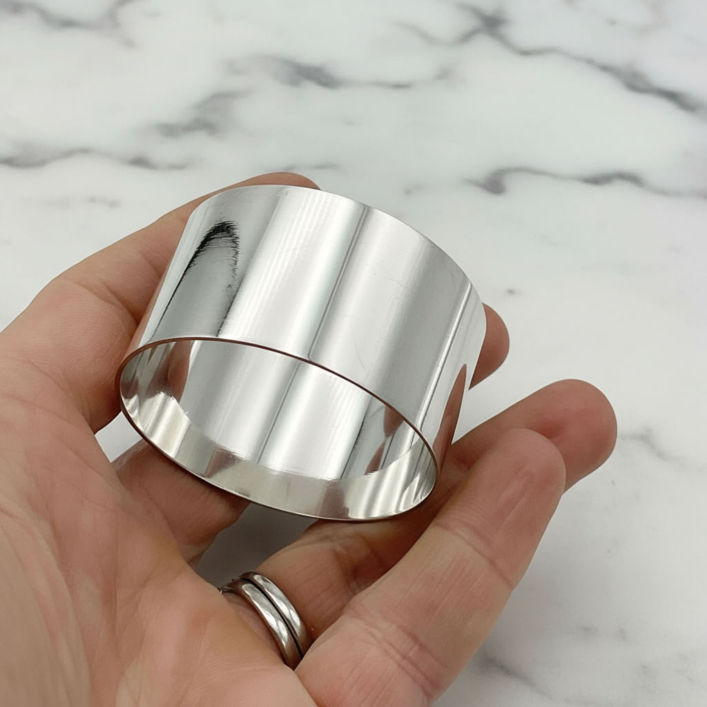 A lovely shiny silver napkin ring held in a hand with a mable background