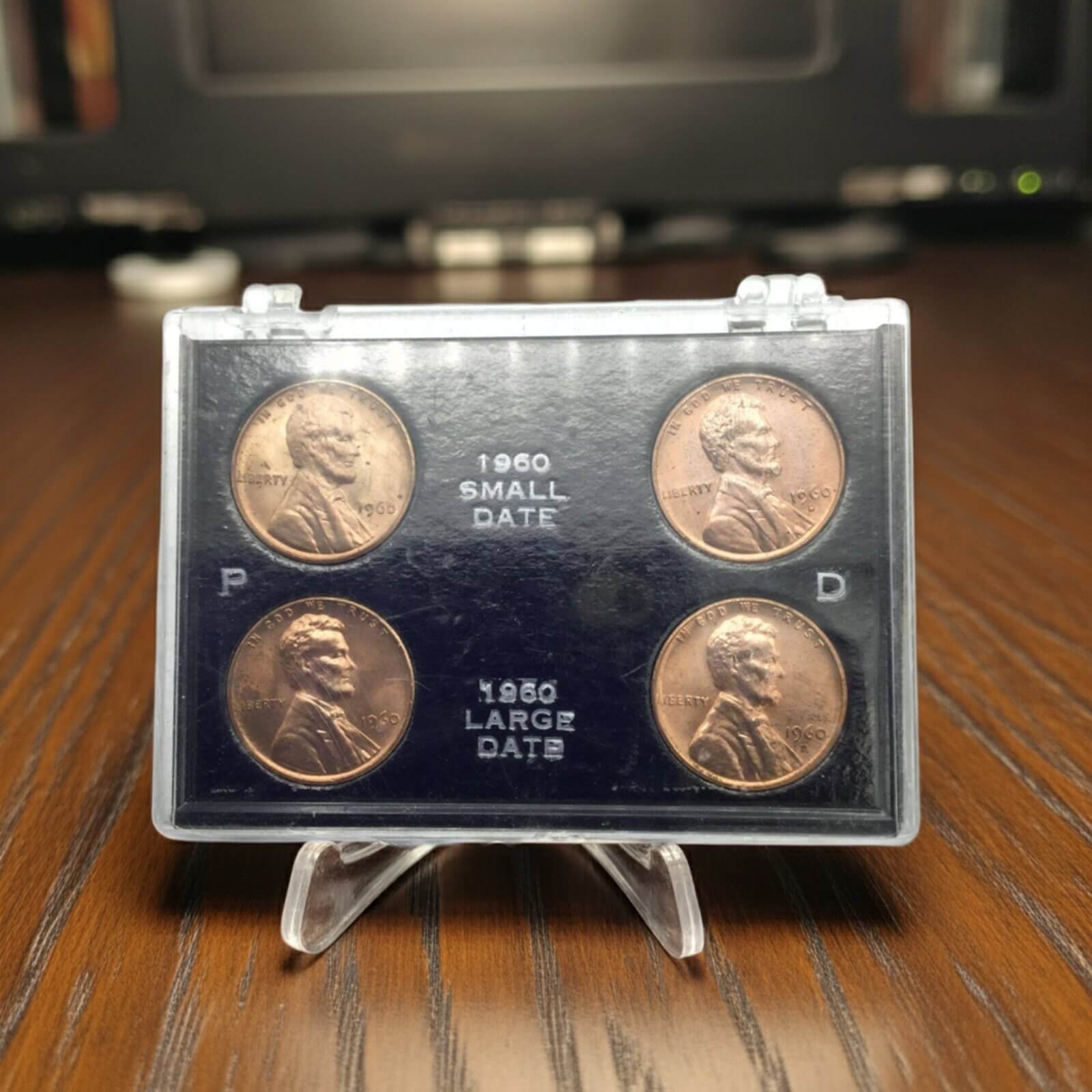 Set of four coins in a display case on a wooden surface with a blurred background