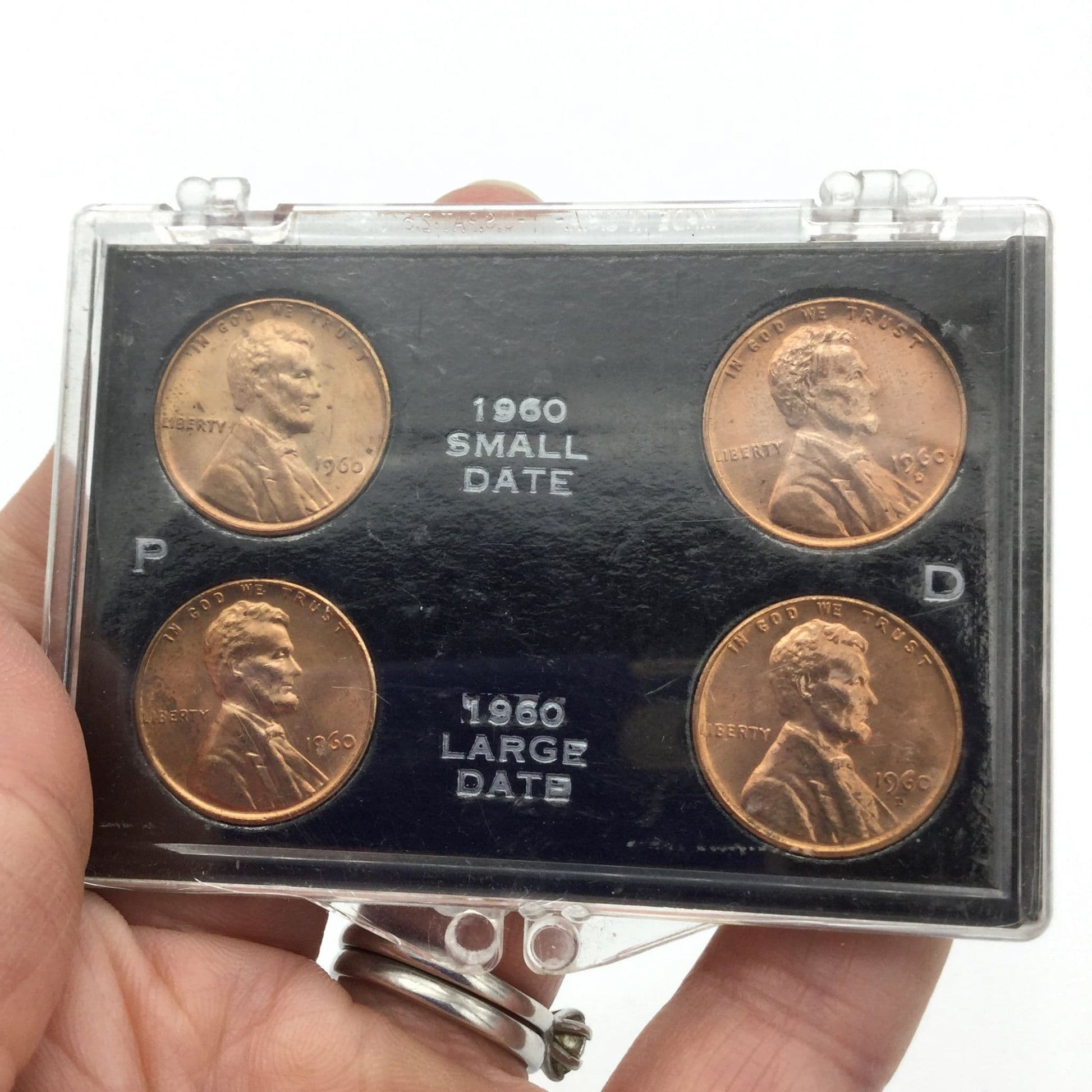 Four Lincoln Memorial Cents in a black holder and perspex case. It has P and D on the blakc holder and 1960 small date and 1960 large date on the black holder held in a hand