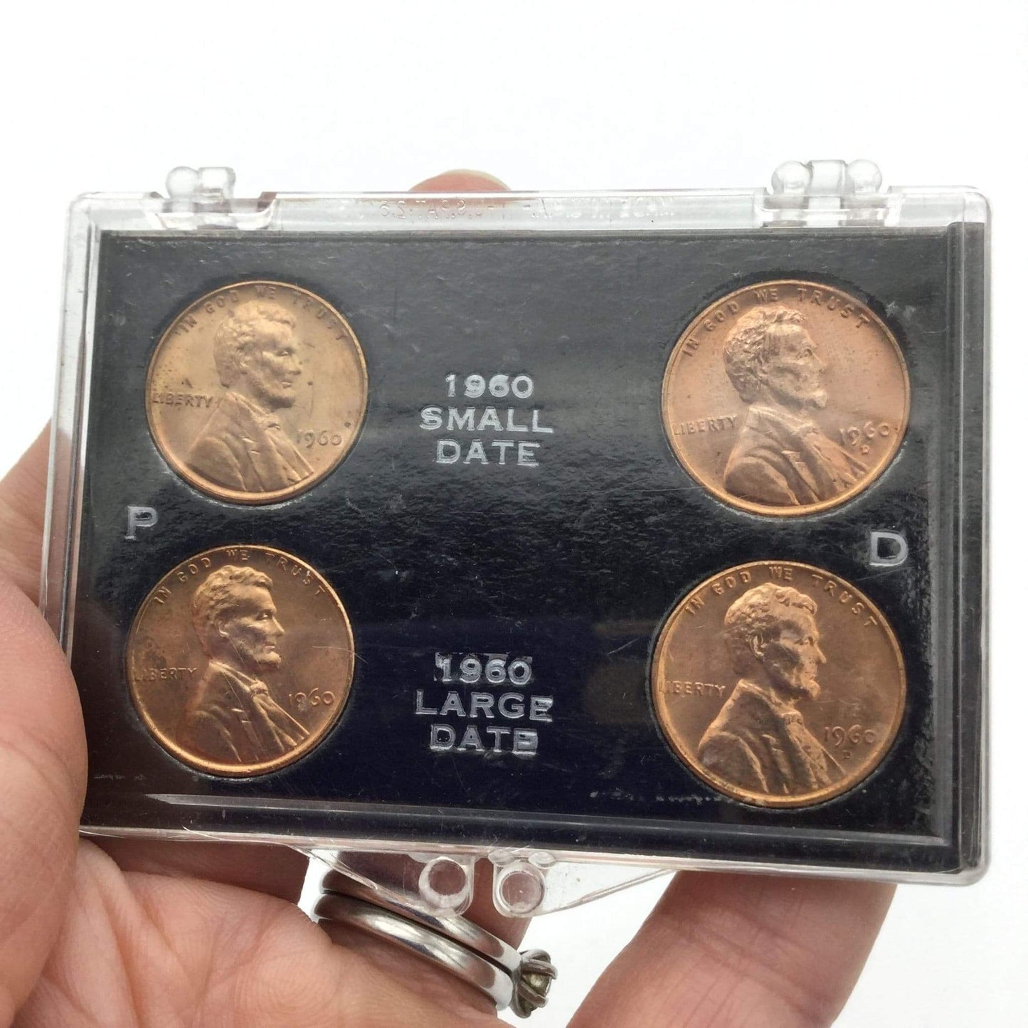 Set of four coins in a display case held by a hand on a white background