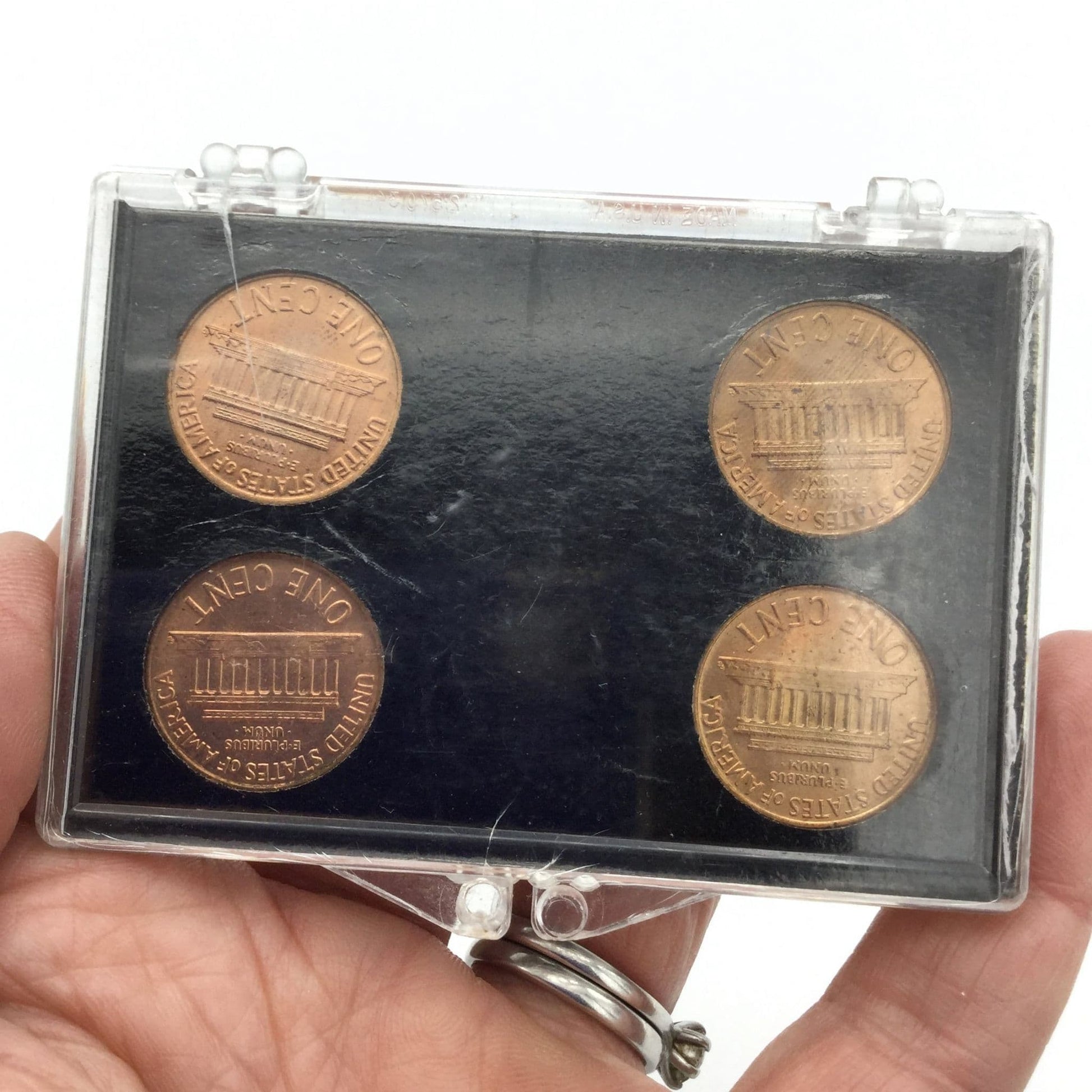Reverse side of Four Lincoln Memorial Cents in a black holder and perspex case. It has P and D on the blakc holder and 1960 small date and 1960 large date on the black holder held in a hand