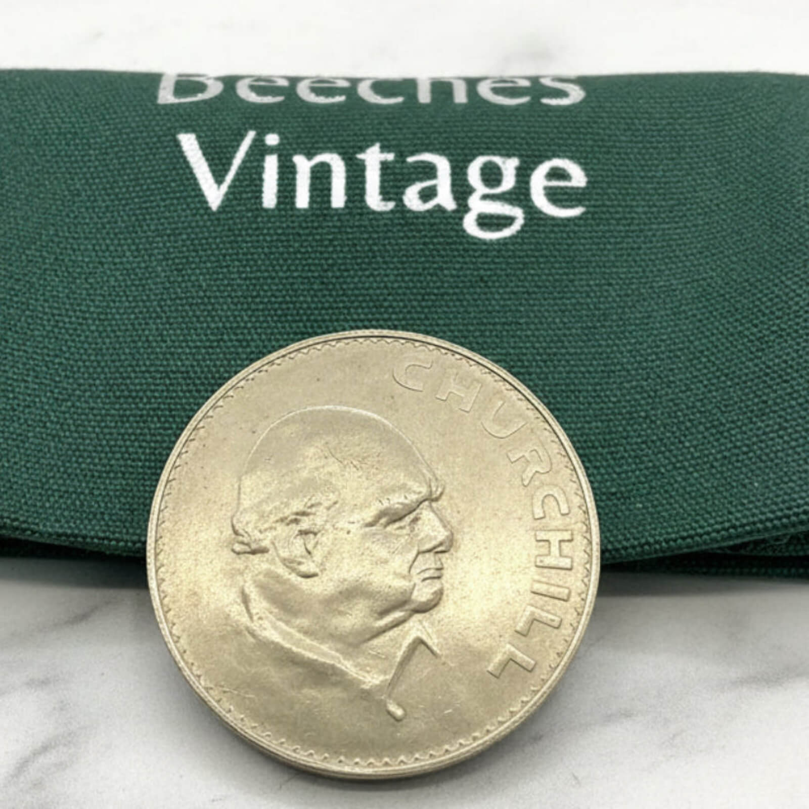 Coin with a portrait on a green fabric background with 'Beeches Vintage' branding.