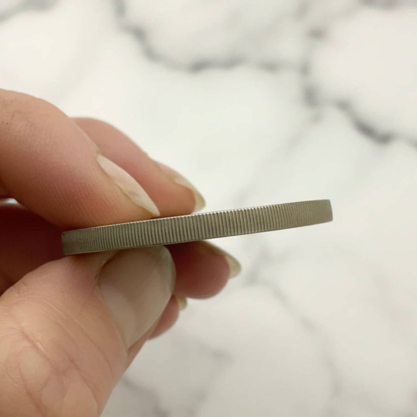 Hand holding a coin side view against a marble background