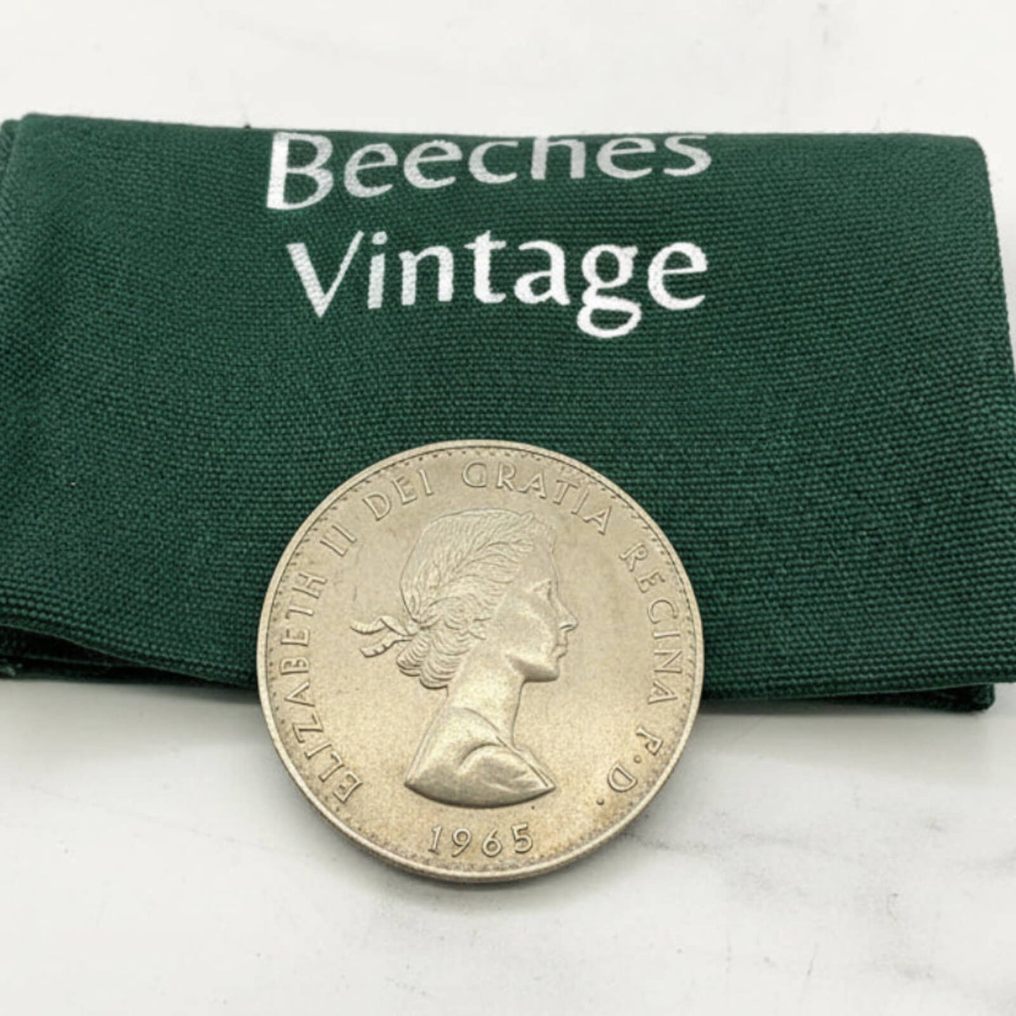Silver coin with a portrait and '1965' on a green 'Beeches Vintage' fabric background