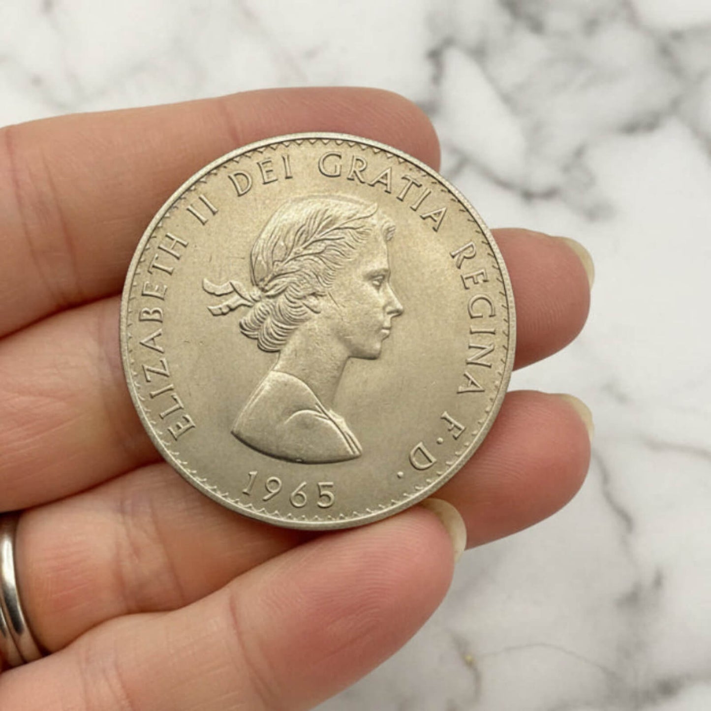 Silver coin with a portrait and text held in a hand against a marble background