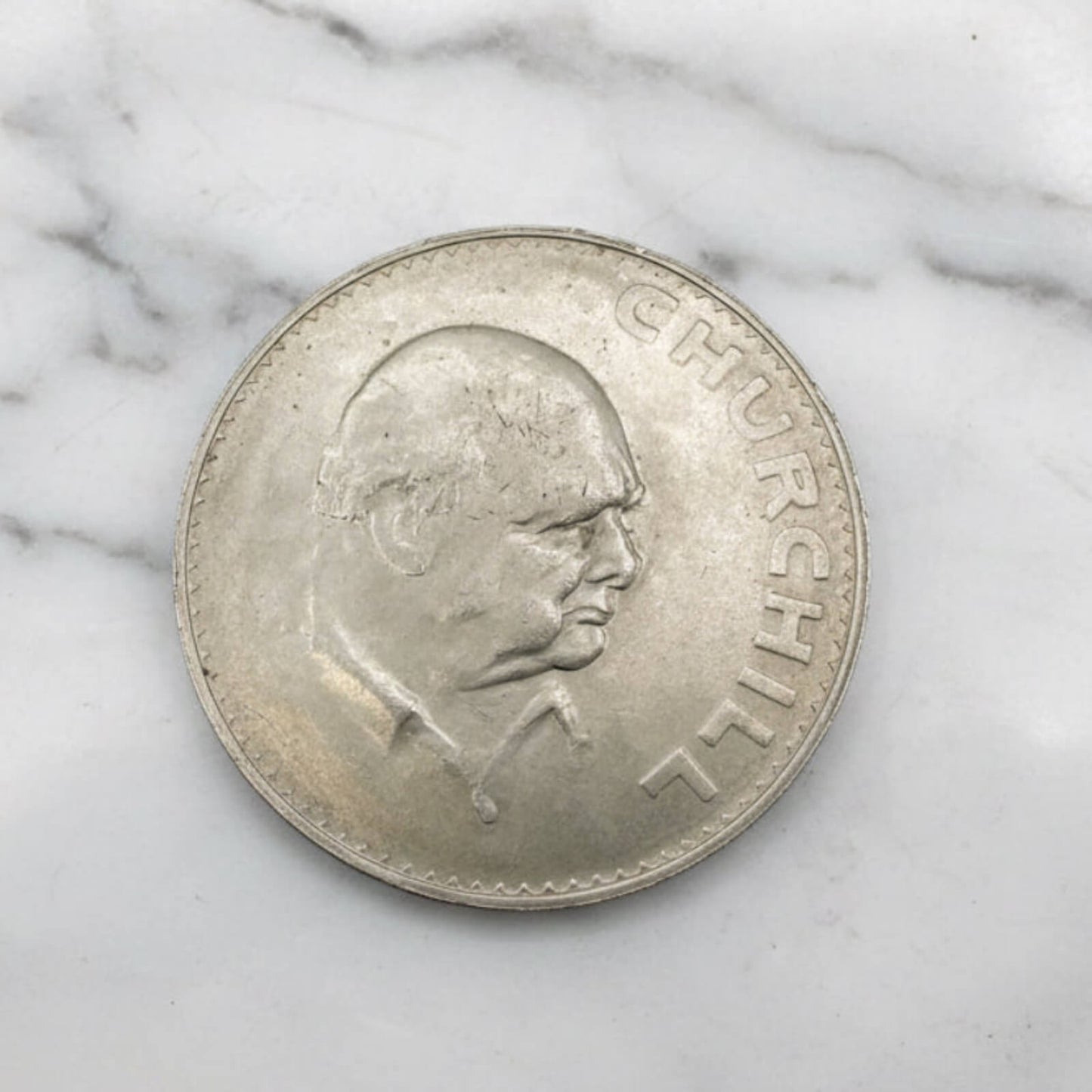 Silver coin with a portrait of Churchill on a marble surface