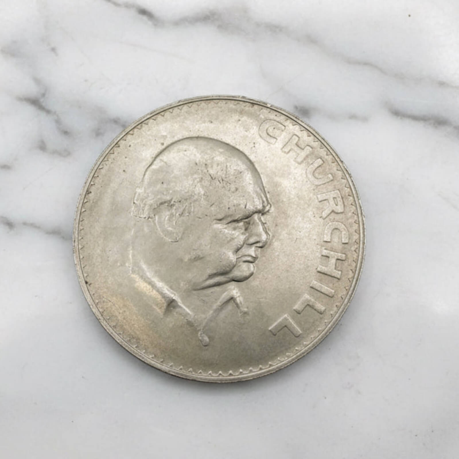 Silver coin with a portrait of Churchill on a marble surface