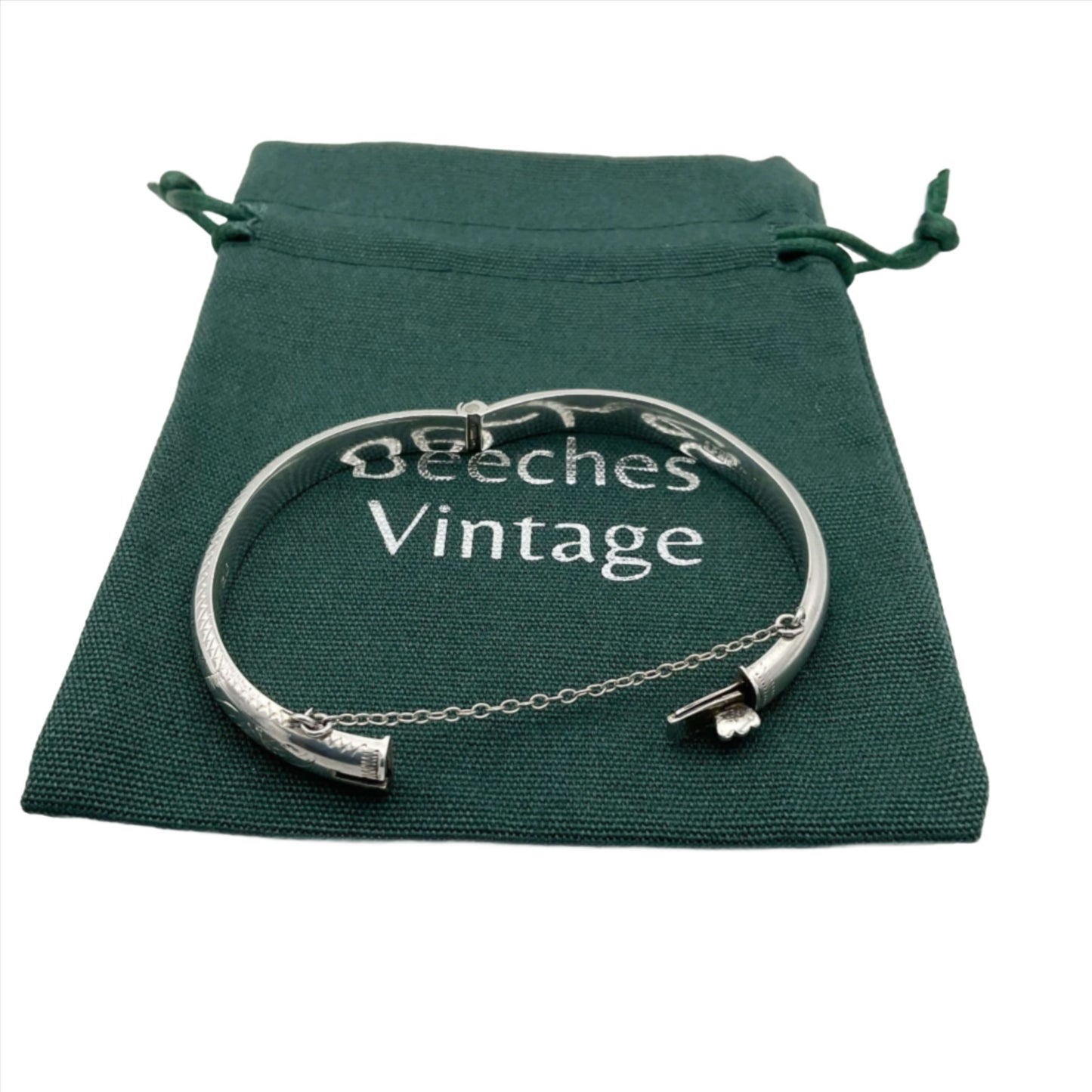 Silver bracelet with etched pattern open showing safety chain on a green bag