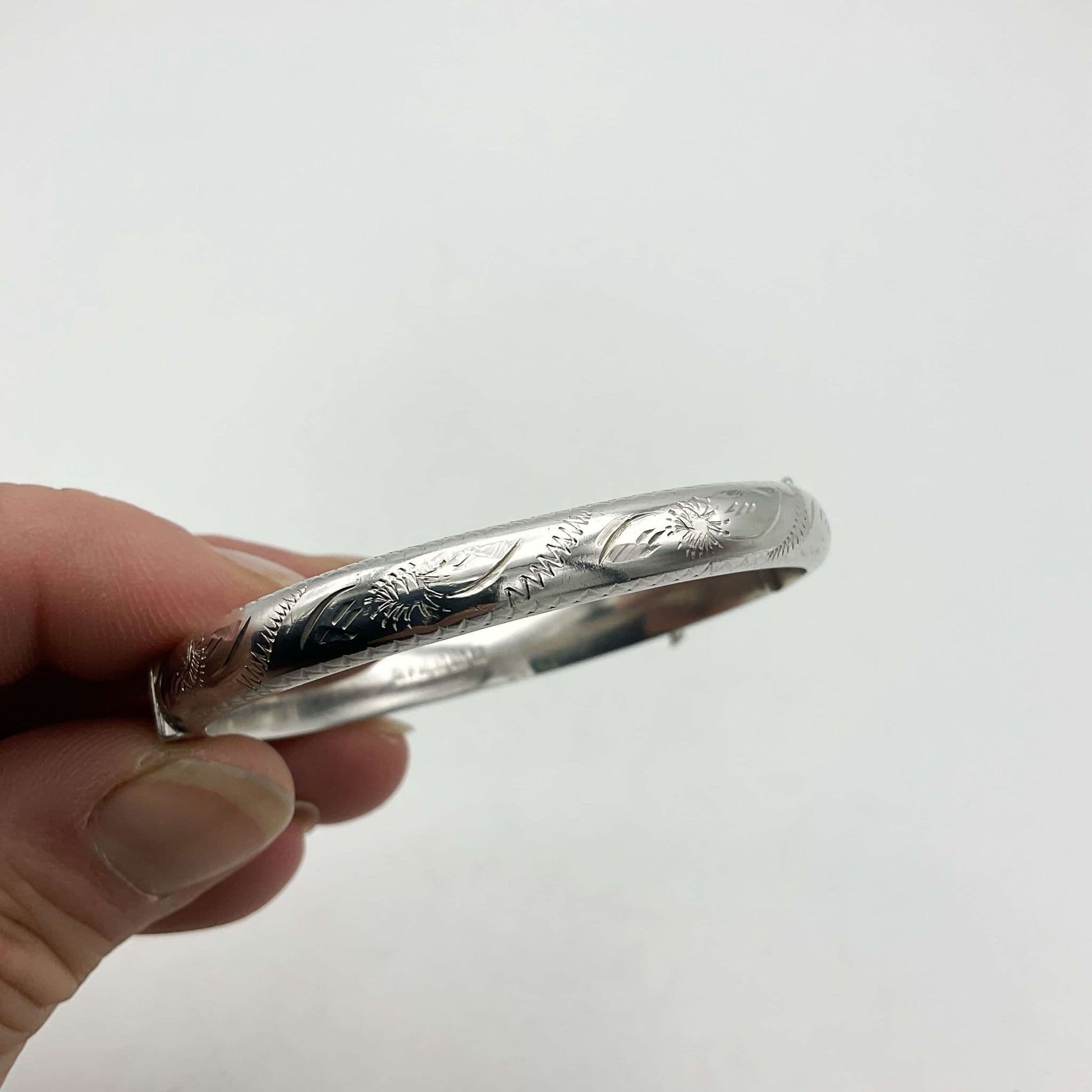 Side view of silver bracelet showing an engraved design held in a hand