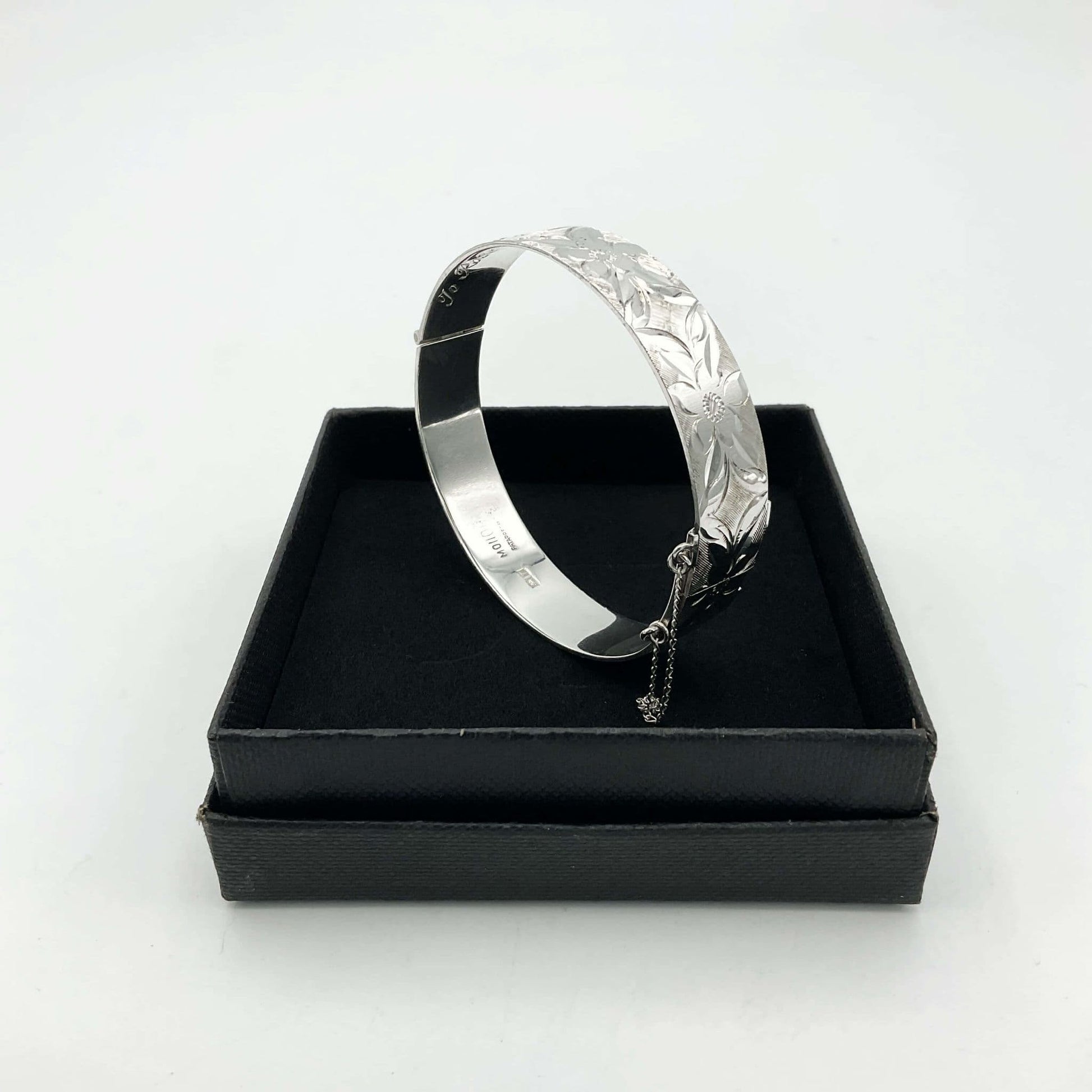 Silver bracelet with engraved flowers sitting inside a black box