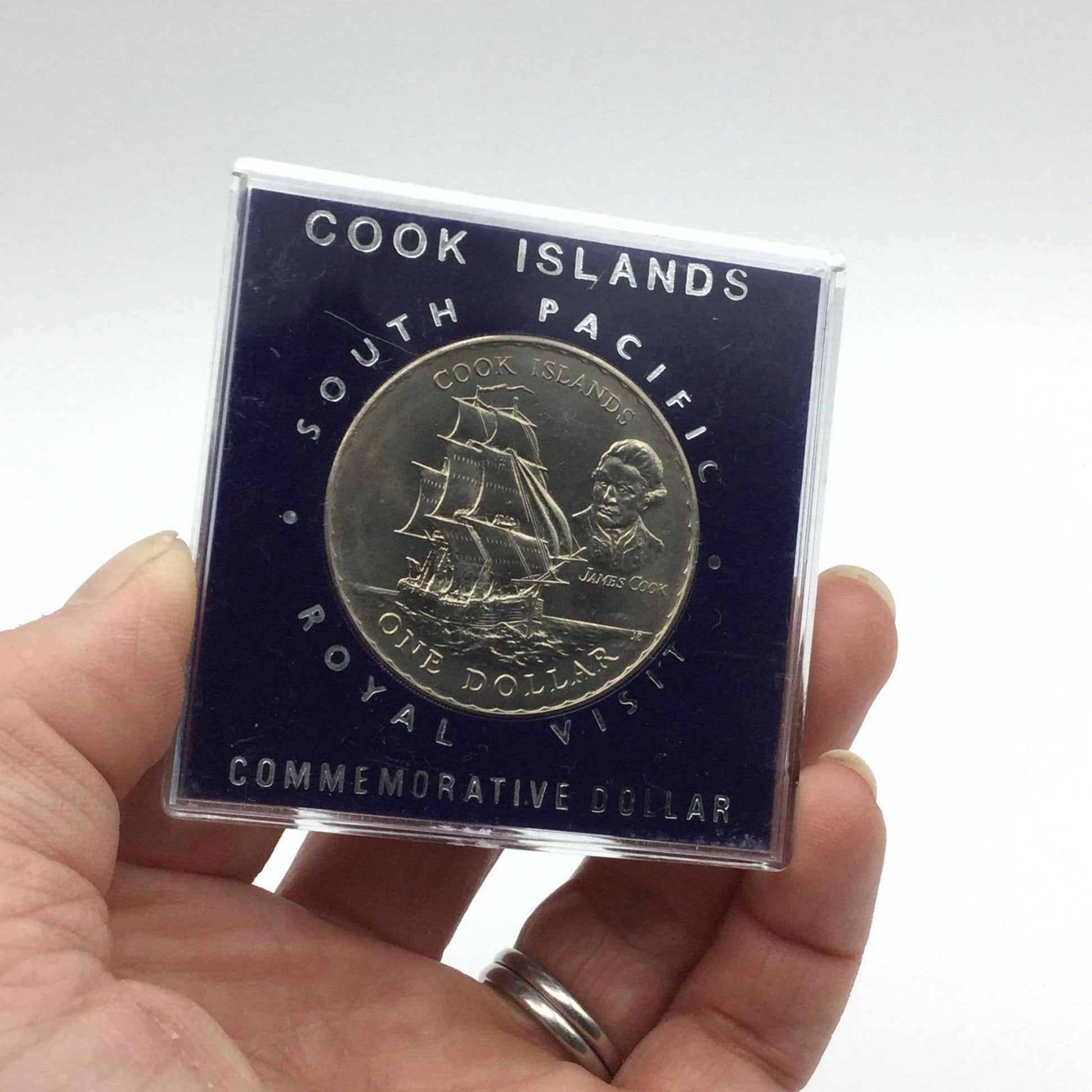 Cook Islands dollar coin with a ship on it in a blue case held in a hand