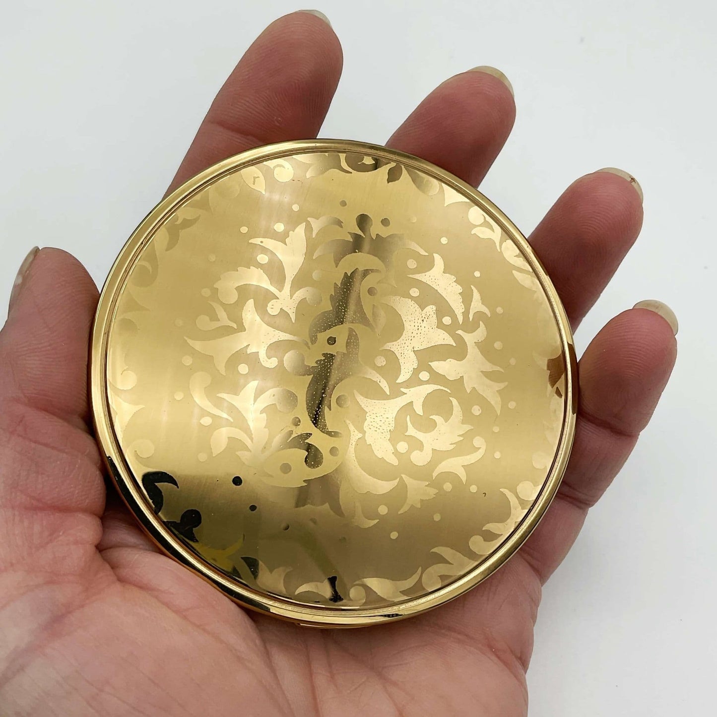 beautiful gold patterned lid of powder compact held in a hand
