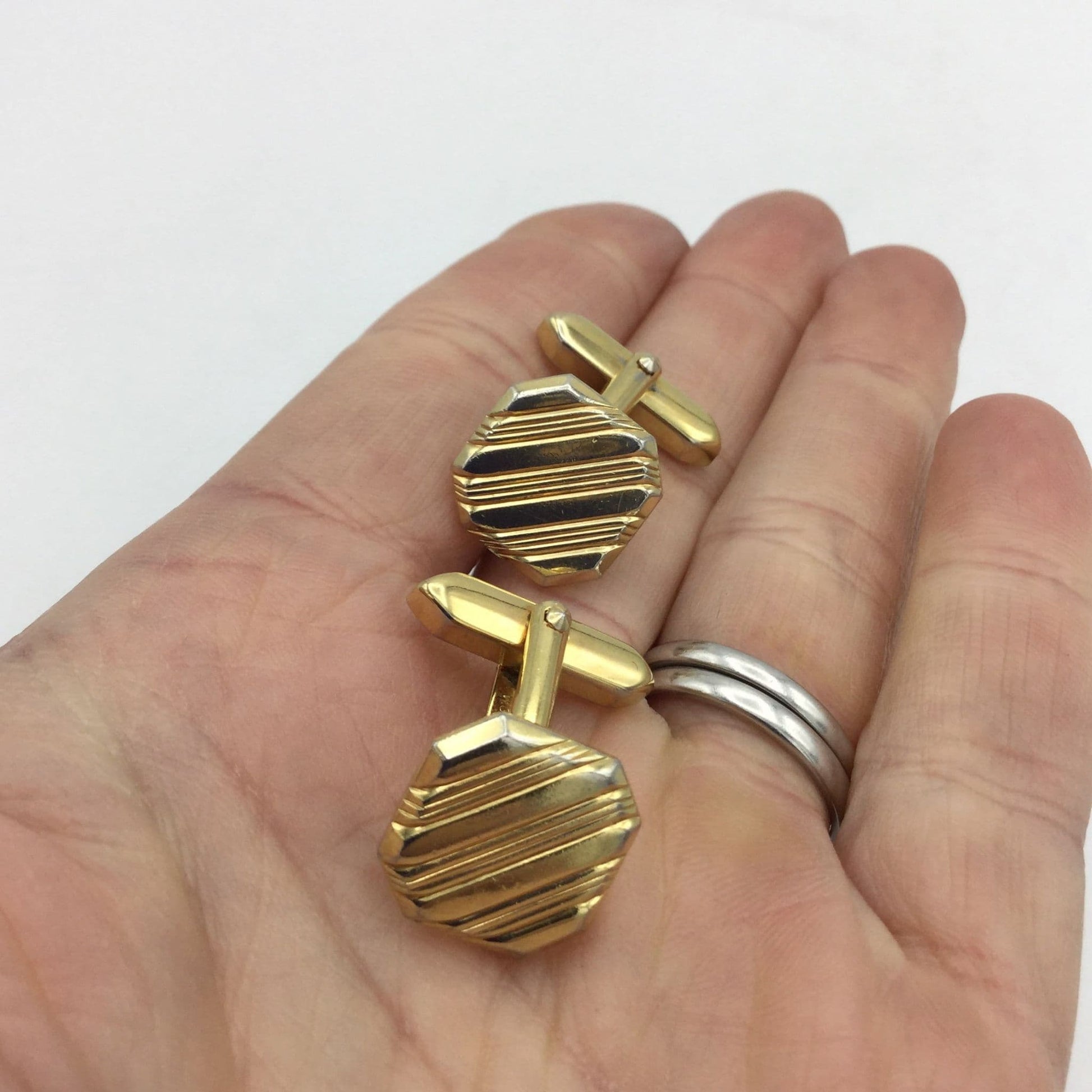 Gilded square cufflinks with a striped pattern held in a hand