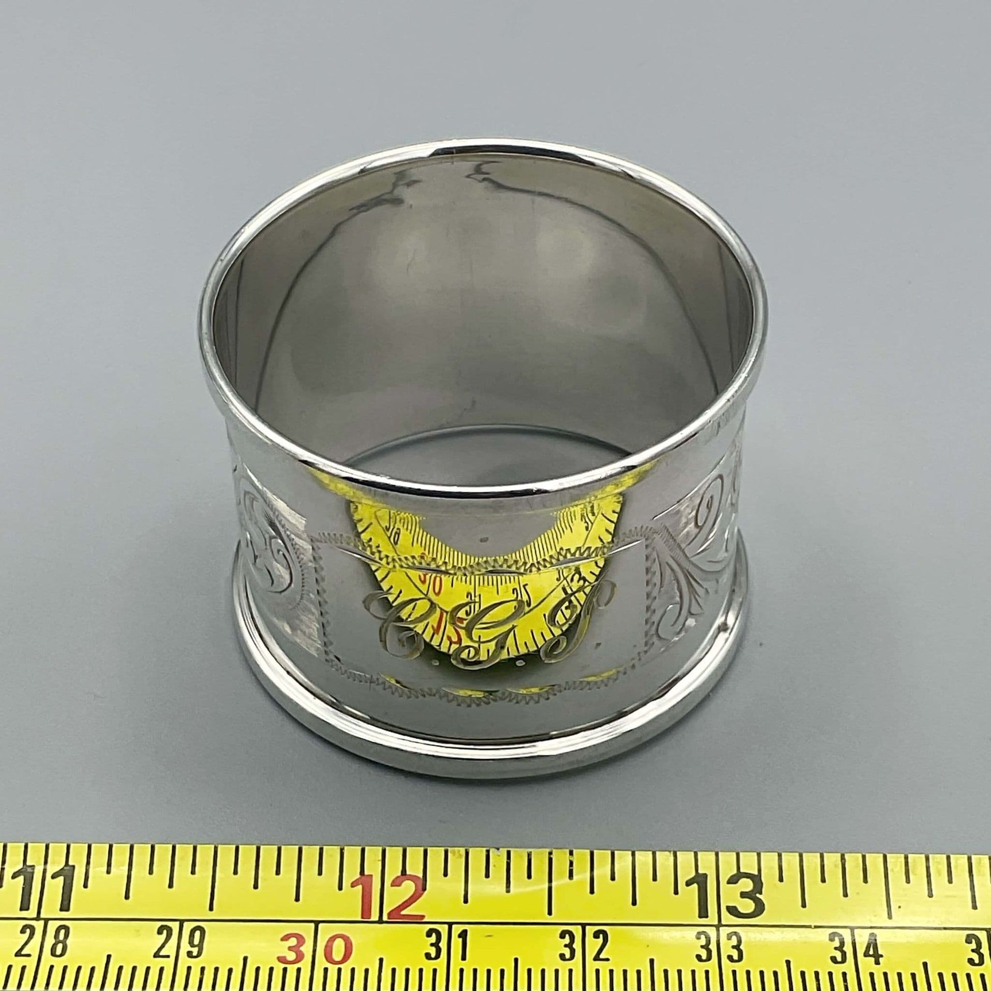 Silver Napkin ring with CGP engraved on the front of it next to a tape measure showing it's size as about 4cm.
