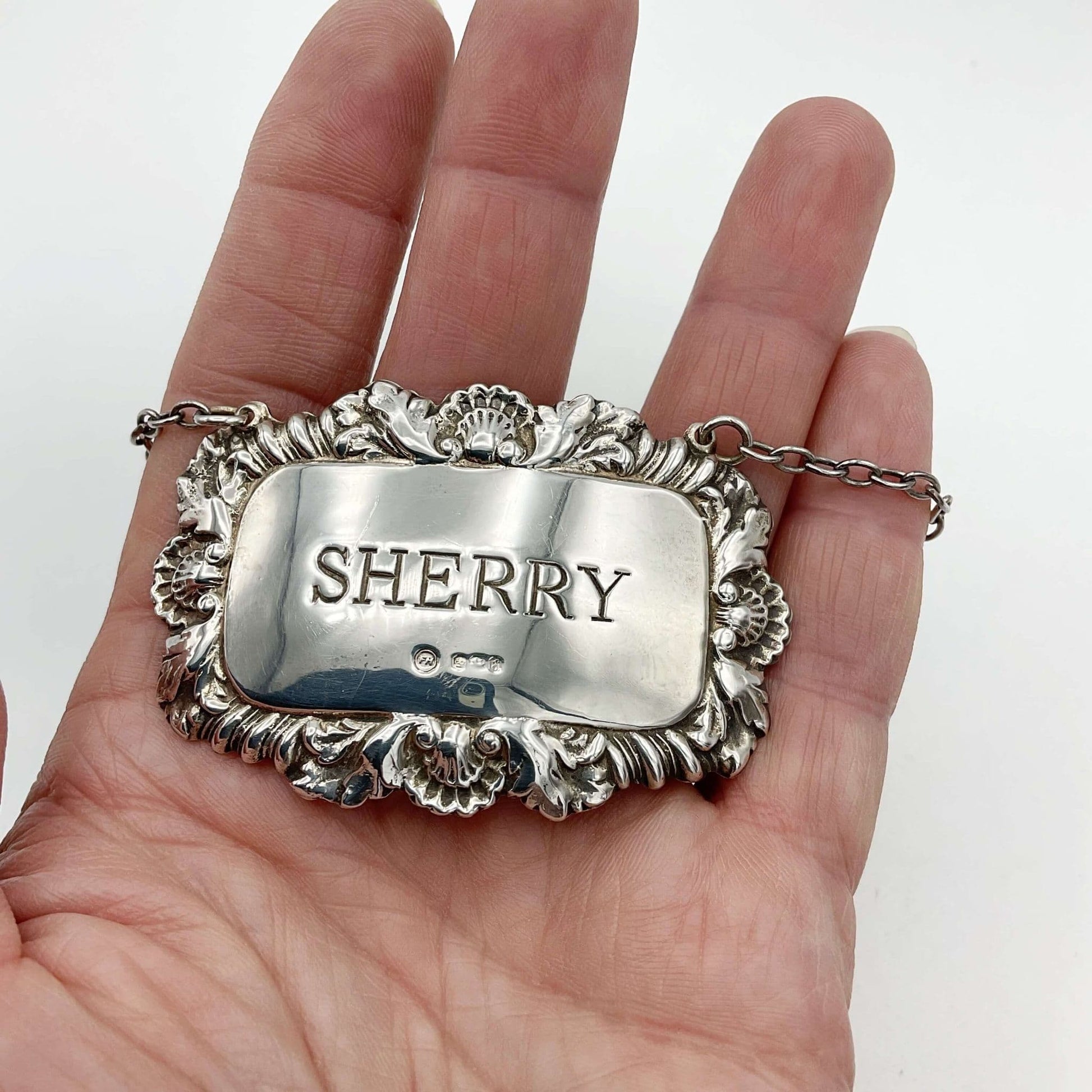 Ornate silver decanter label with Sherry engraved in the centre held in a hand