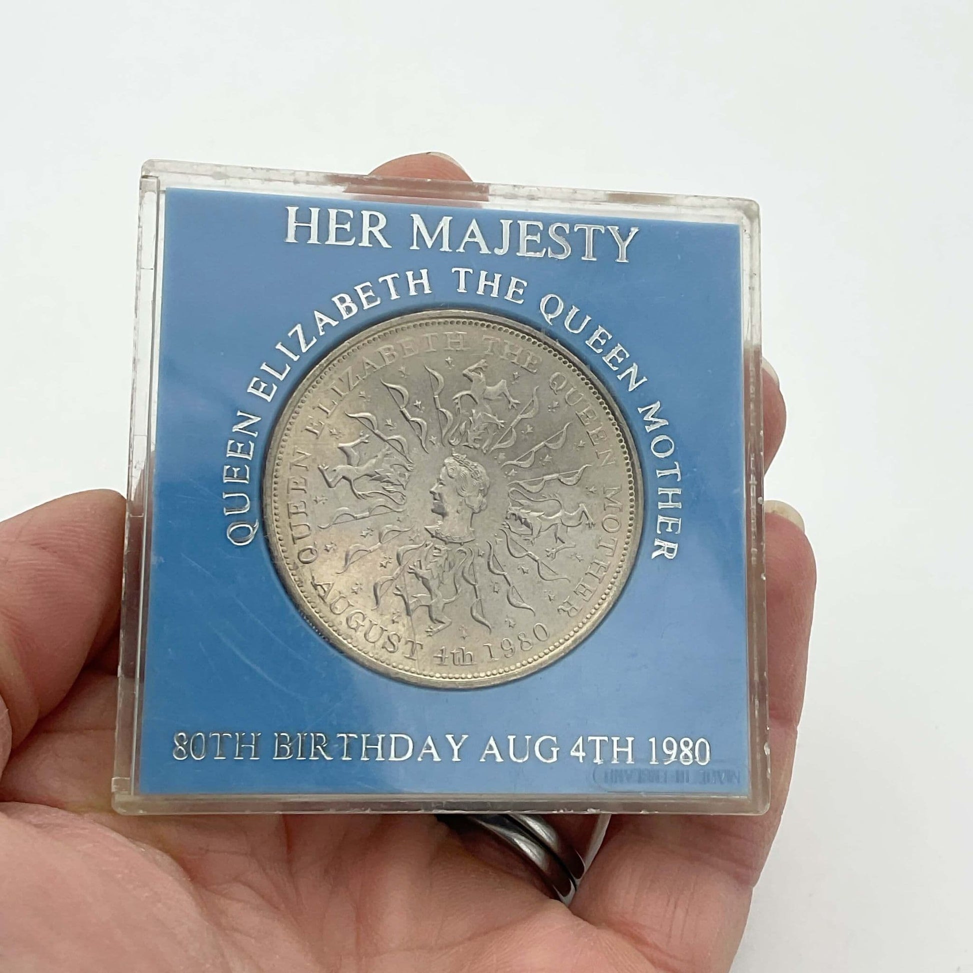 Silver coin featuring the Queen Mother's head in a light blue case held in a hand