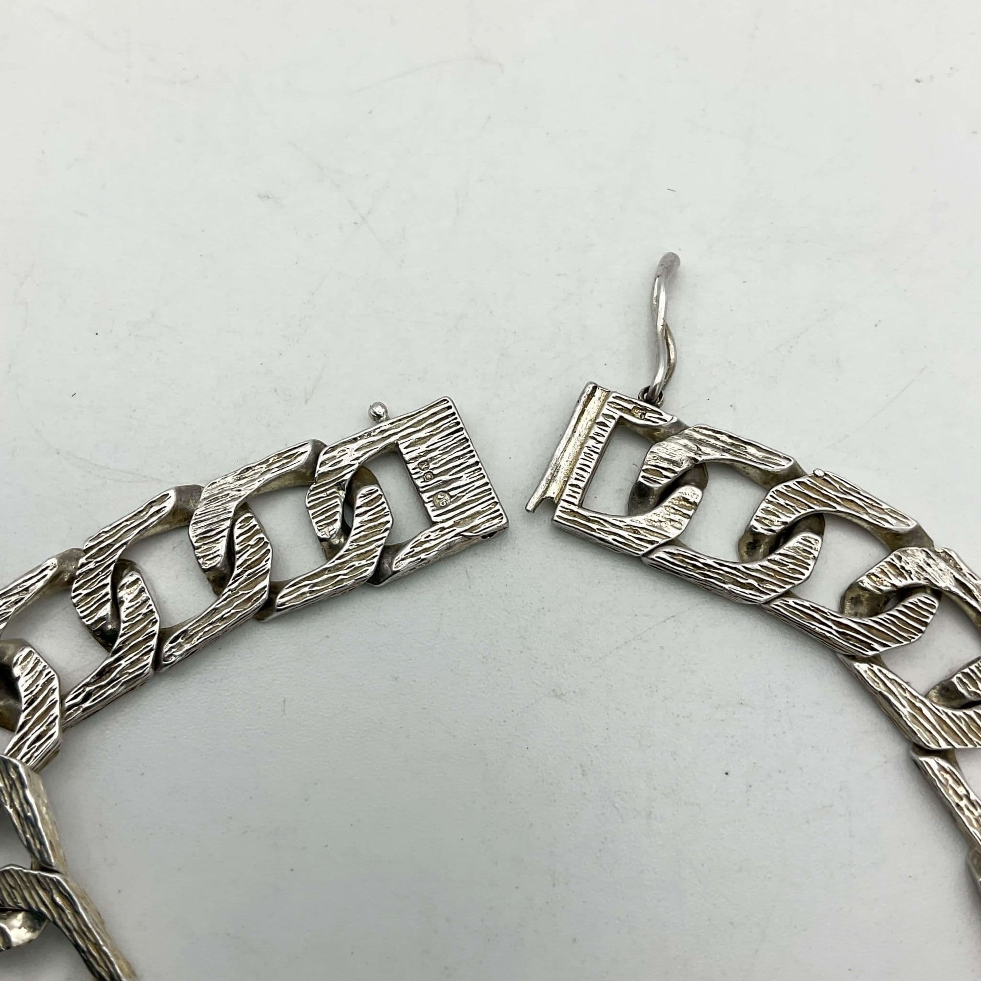 The clasp of the silver chain bracelet lying flat on a white background