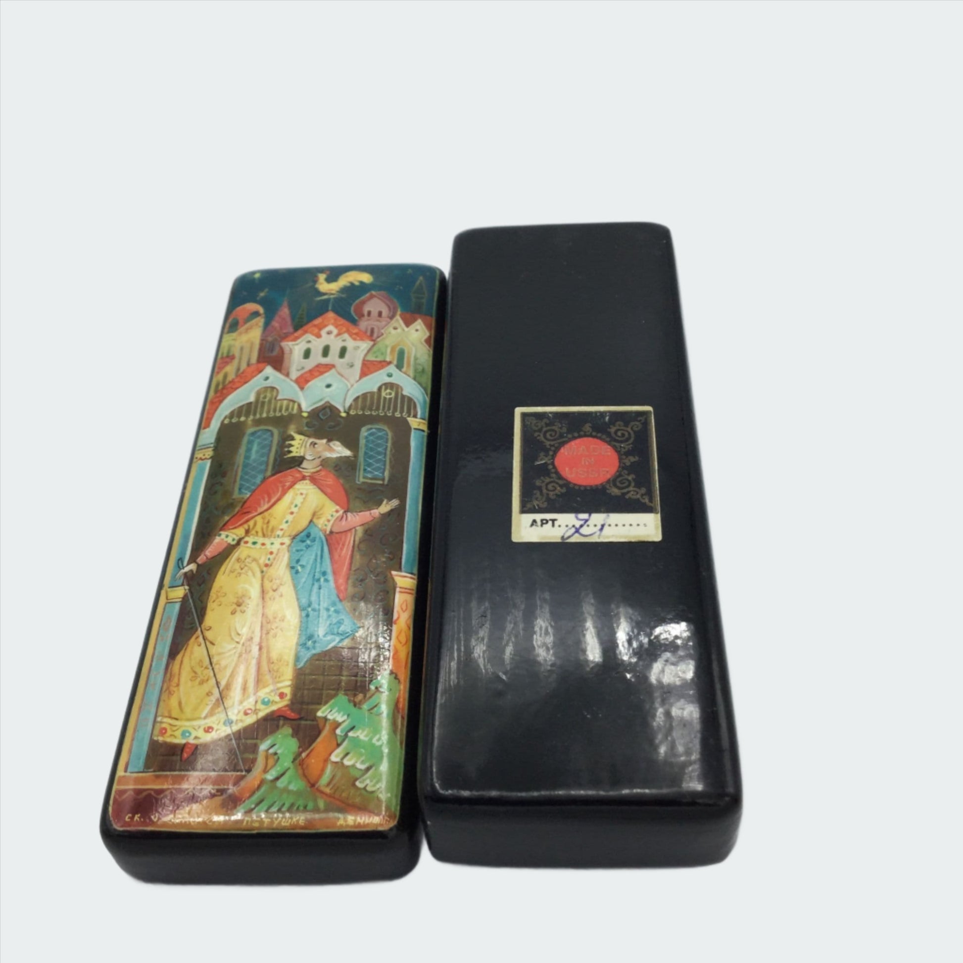 Black handpainted box with a colourful painting of a king looking at a cockerel above him and the base with the Apt 21 sticker on it