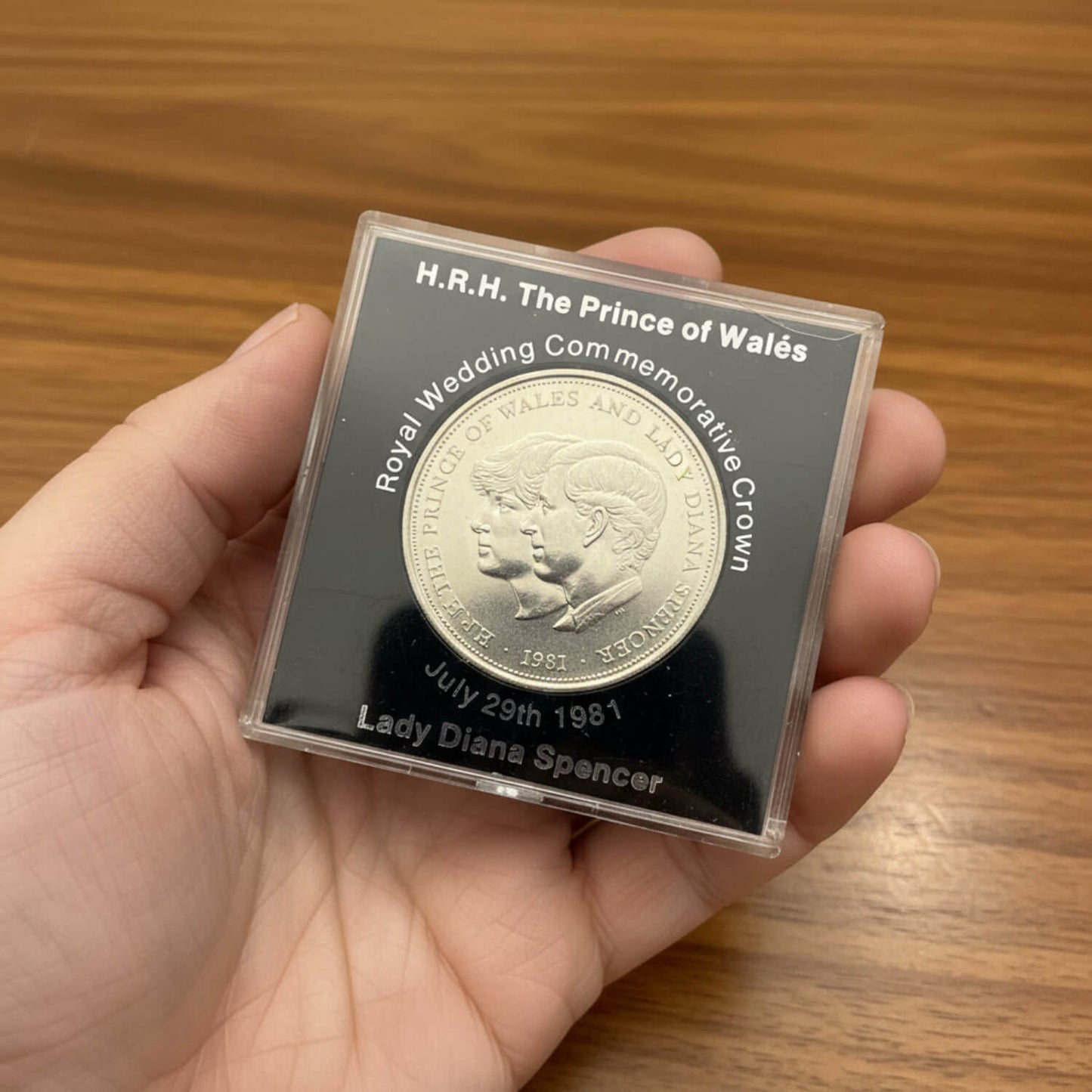 Silver coin in a protective case held by a hand on a wooden surface
