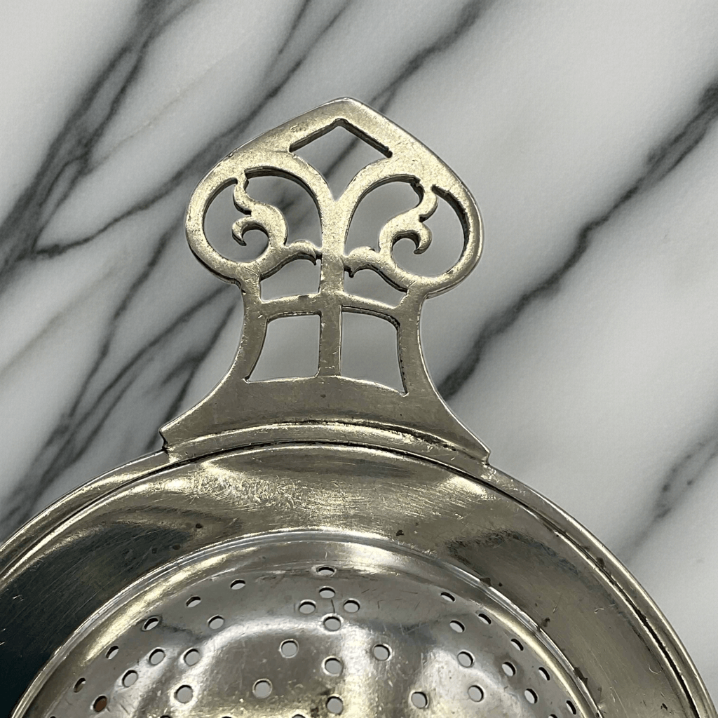 Silver tea strainer with decorative top on a marble background