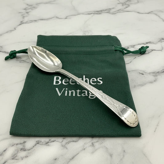 Silver spoon on a green drawstring bag with 'Beeches Vintage' text on a marble background