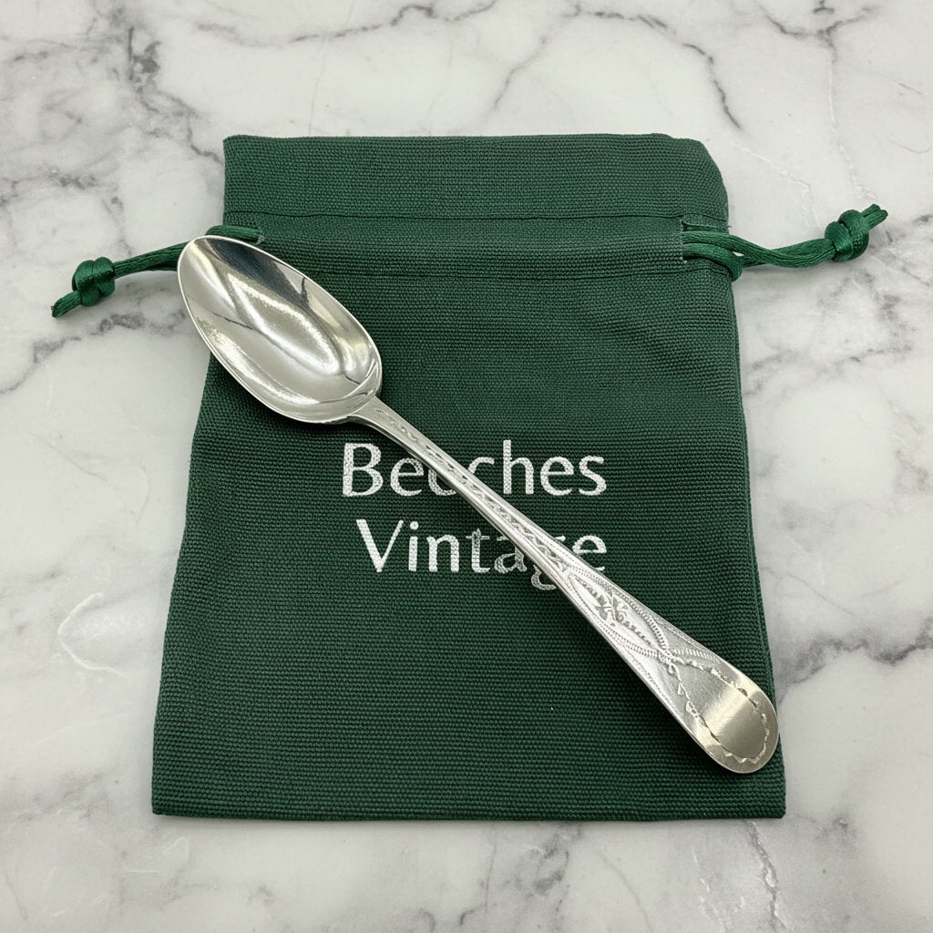 Silver spoon on a green drawstring bag with 'Beeches Vintage' text on a marble background