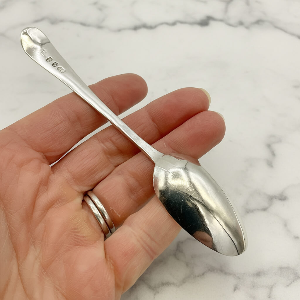 Silver spoon held in a hand against a marble background