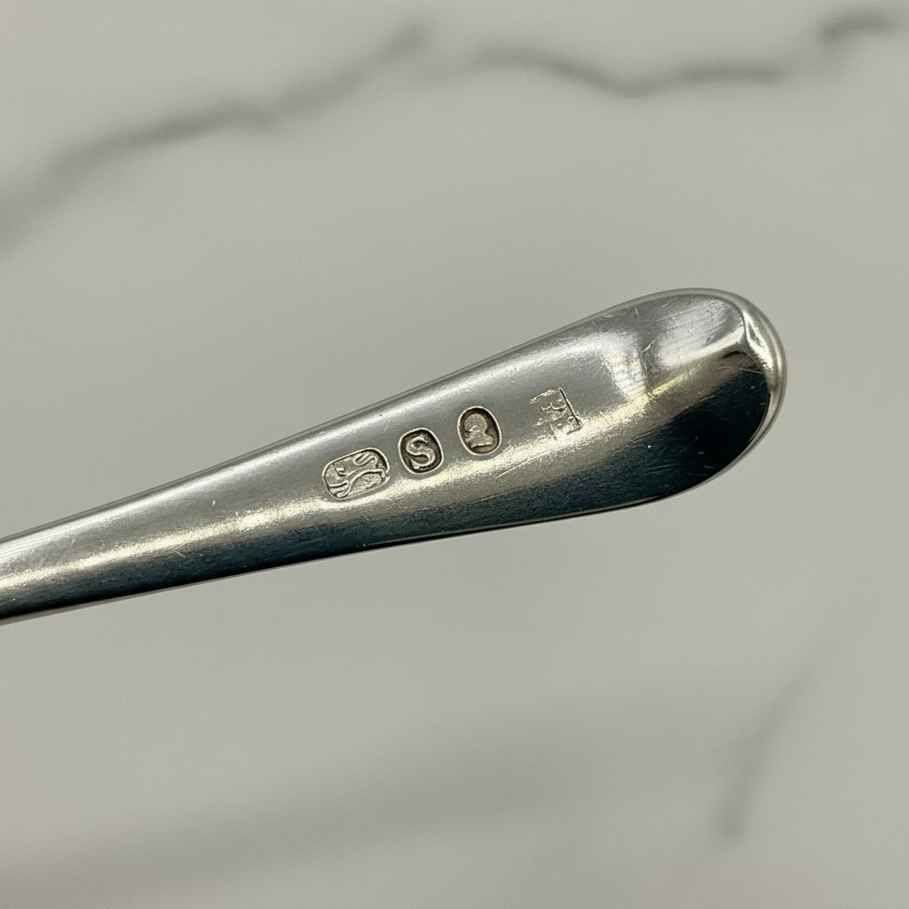 Close-up of a silver spoon with visible hallmarks on a light marble background