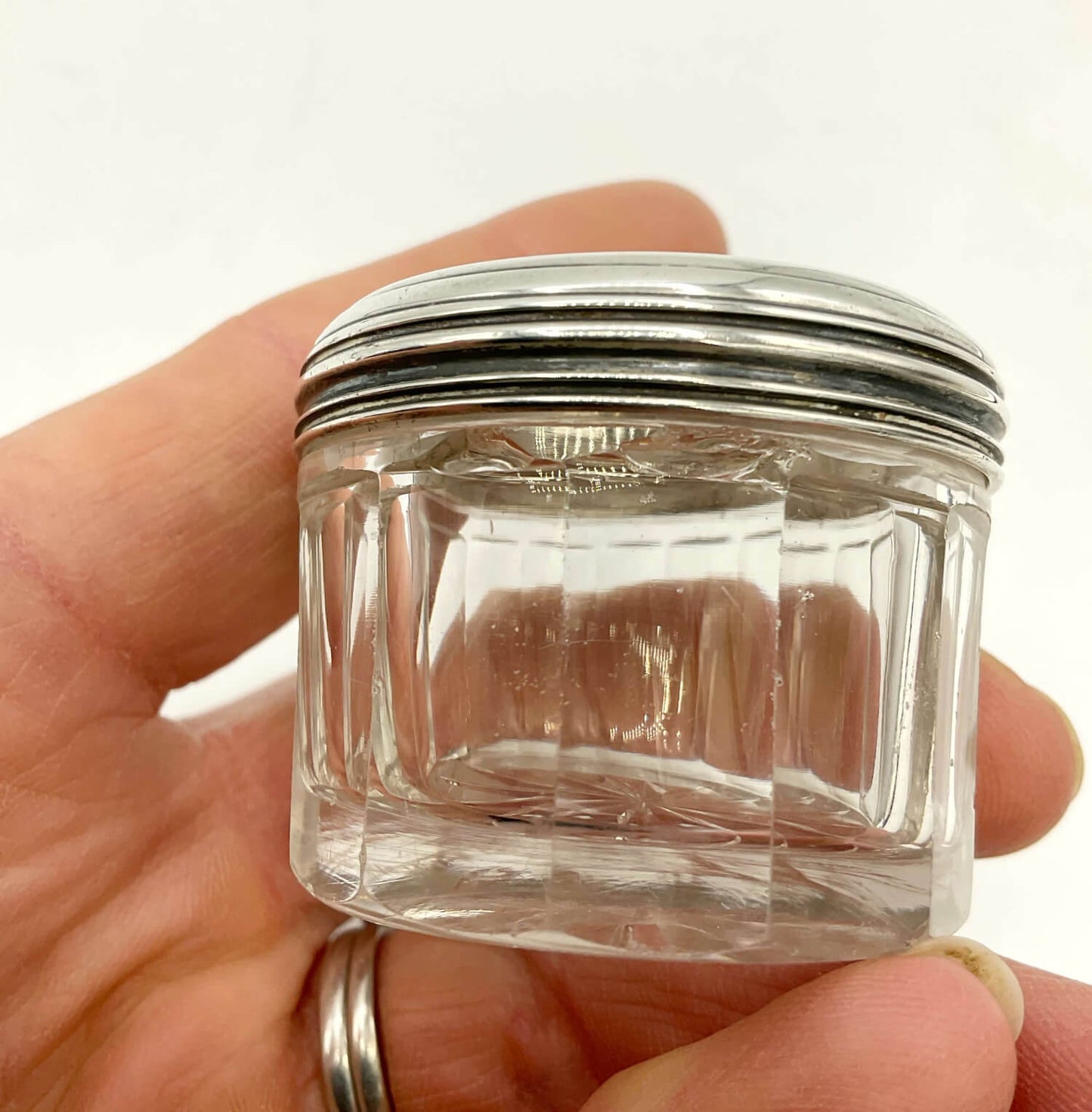 Small clear glass jar with a silver lid held in a hand against a white background