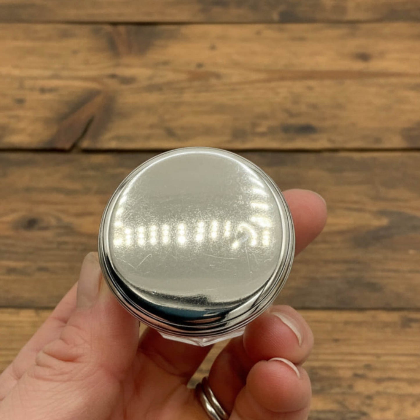 Silver round jar held by a hand on a wooden surface