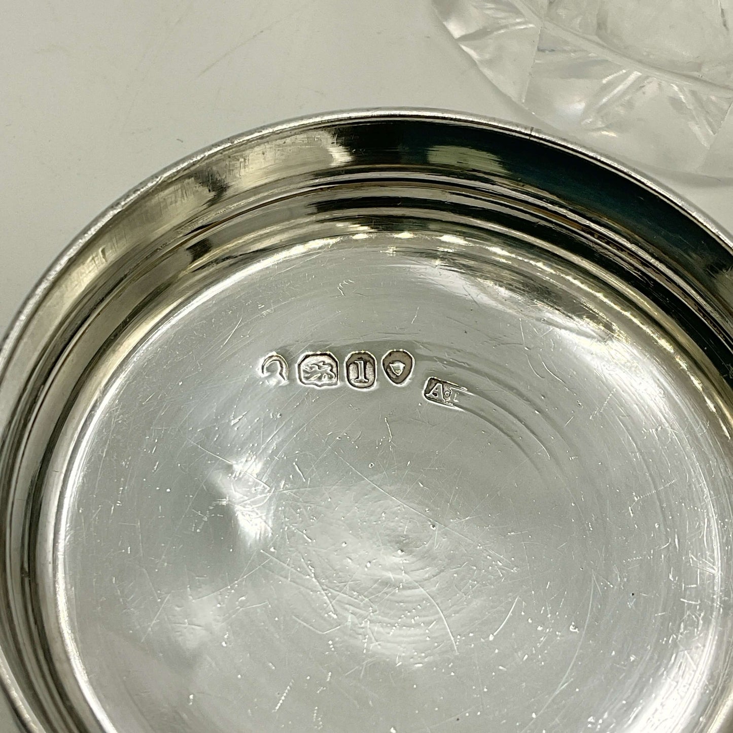 Close-up of a silver lid with visible hallmarks on a white surface
