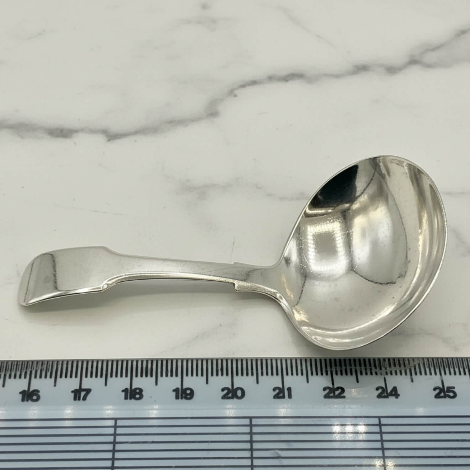 Antique 1800s Silver Tea Caddy Spoon next to a ruler for scale on a marble worktop