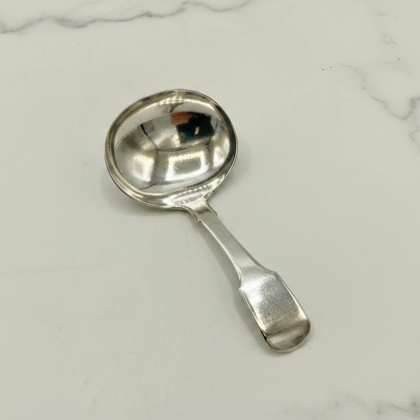 Antique 1800s Silver Tea Caddy Spoon on a marble surface