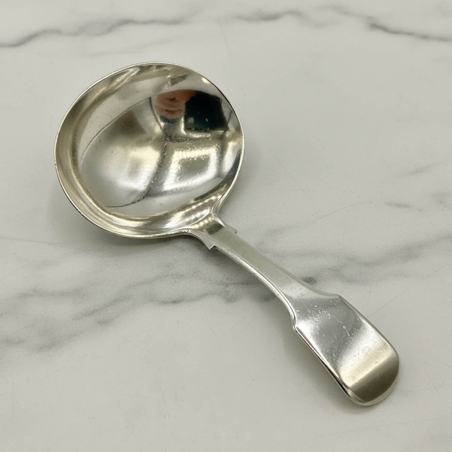 Antique 1800s Silver Tea Caddy Spoon on  a marble surface