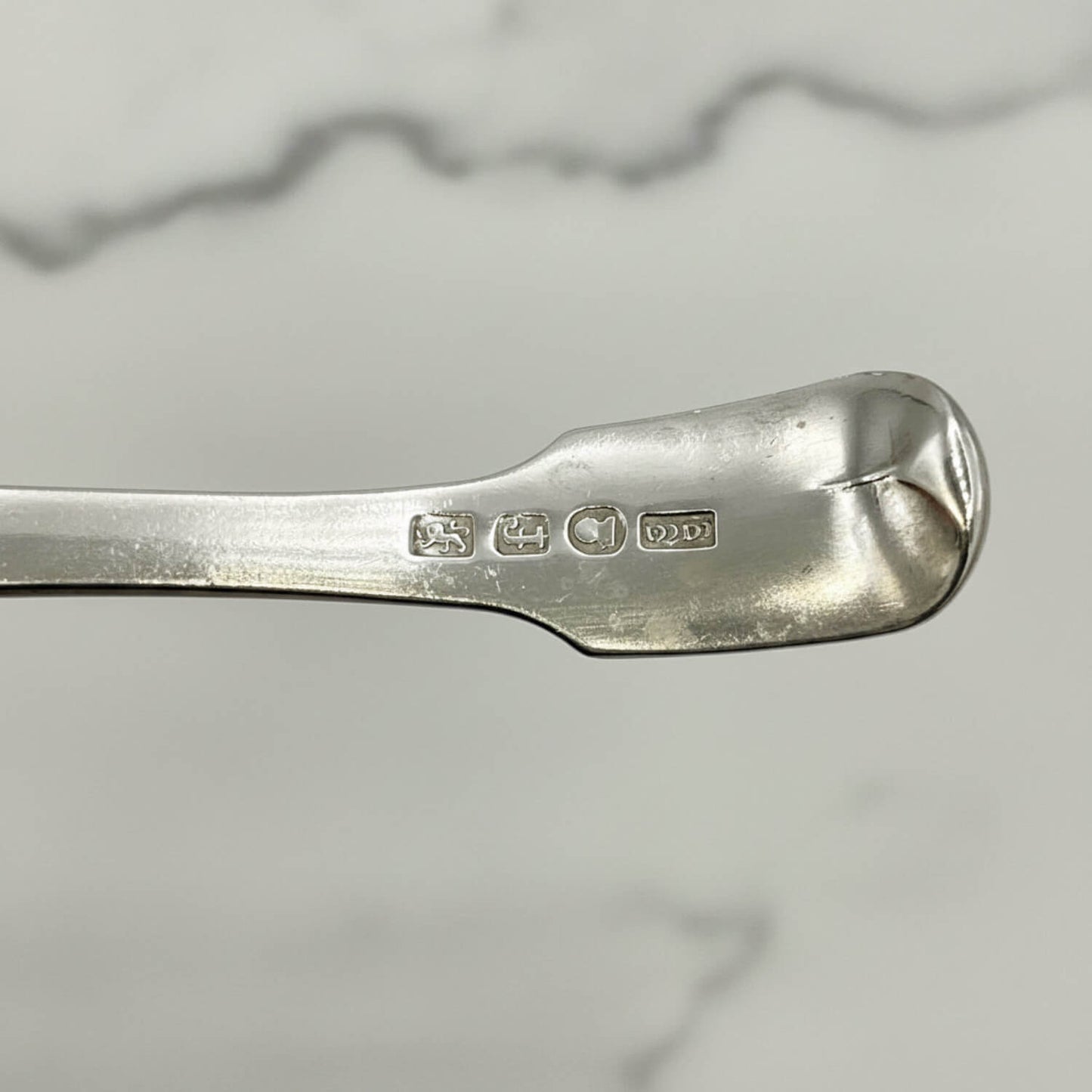 Antique 1800s Silver Tea Caddy Spoon with hallmarks and a marble surface in the background