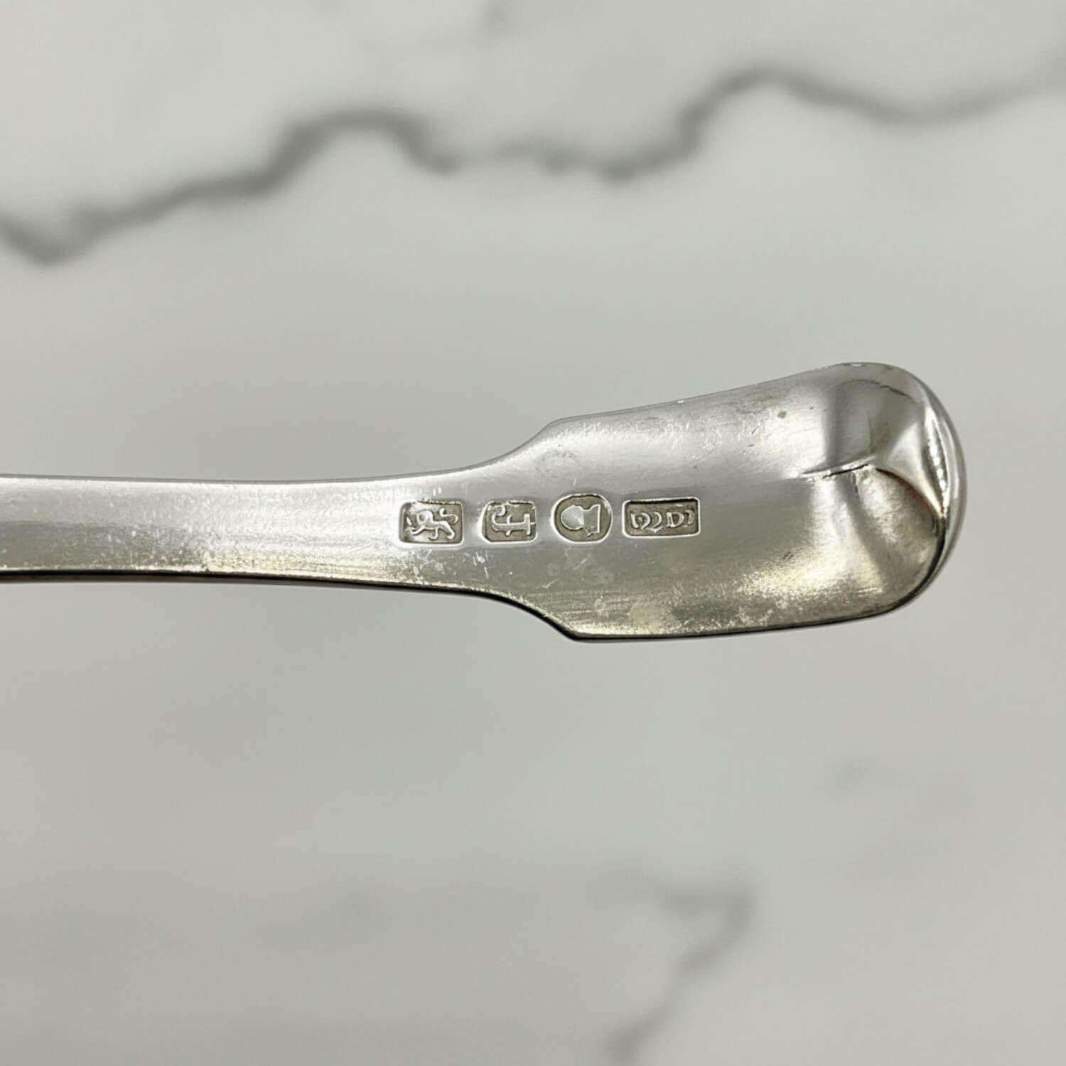 Antique 1800s Silver Tea Caddy Spoon with hallmarks and a marble surface in the background
