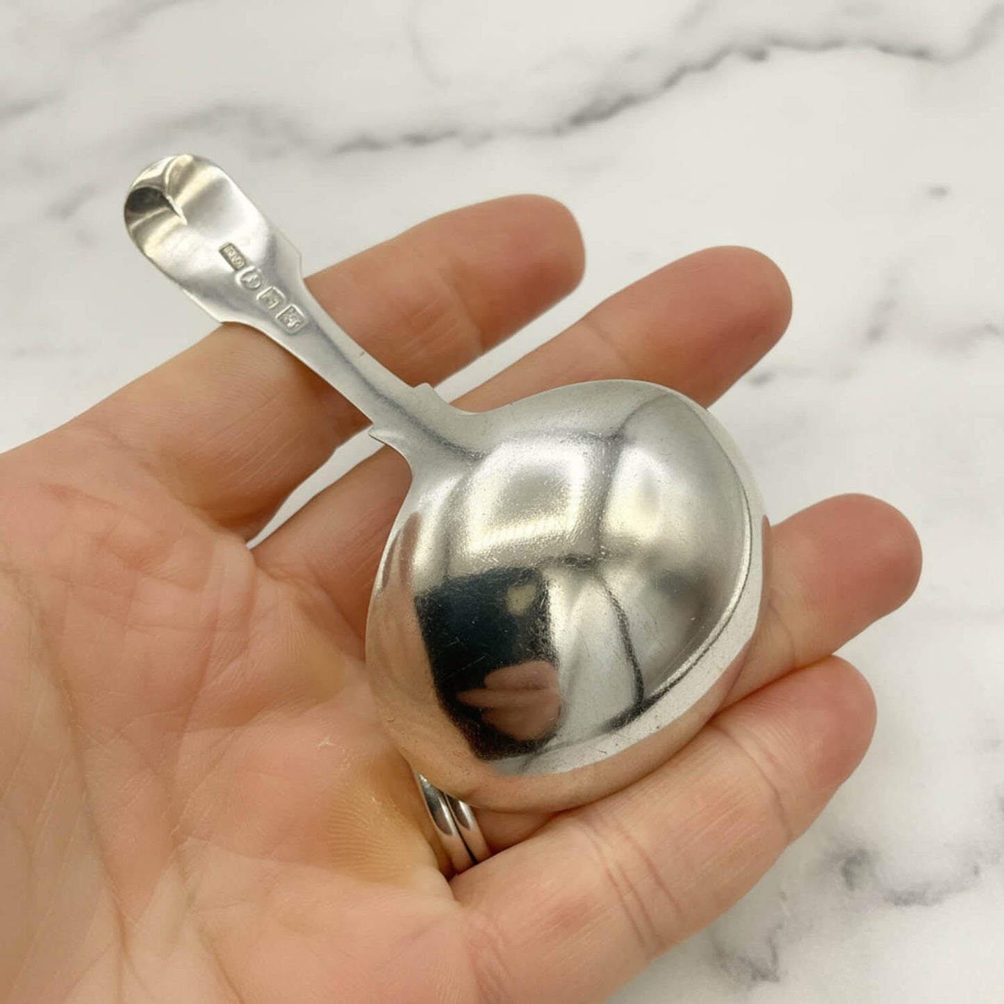 Silver tea caddy spoon held in a hand against a marble background