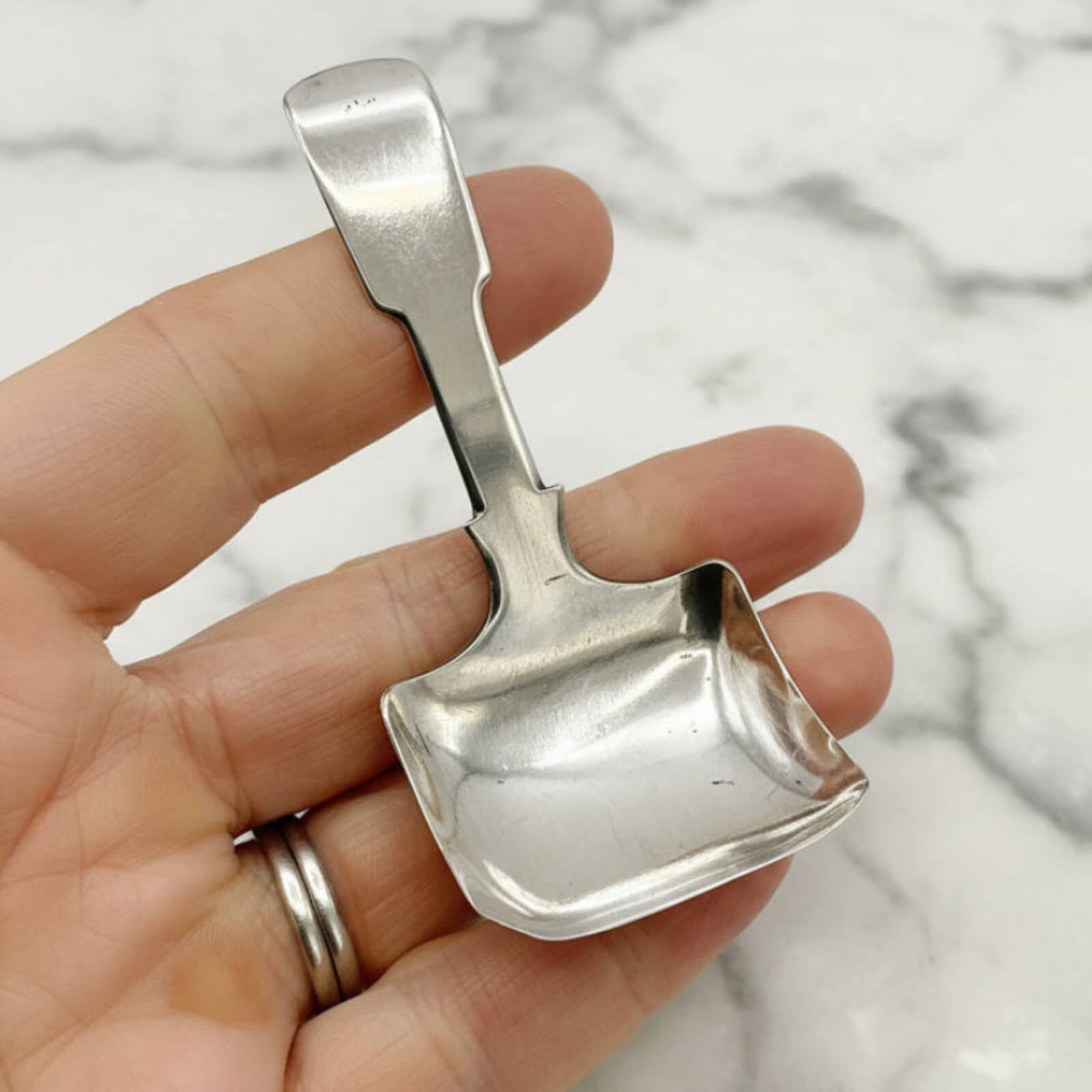 Small silver scoop held in a hand against a marble background